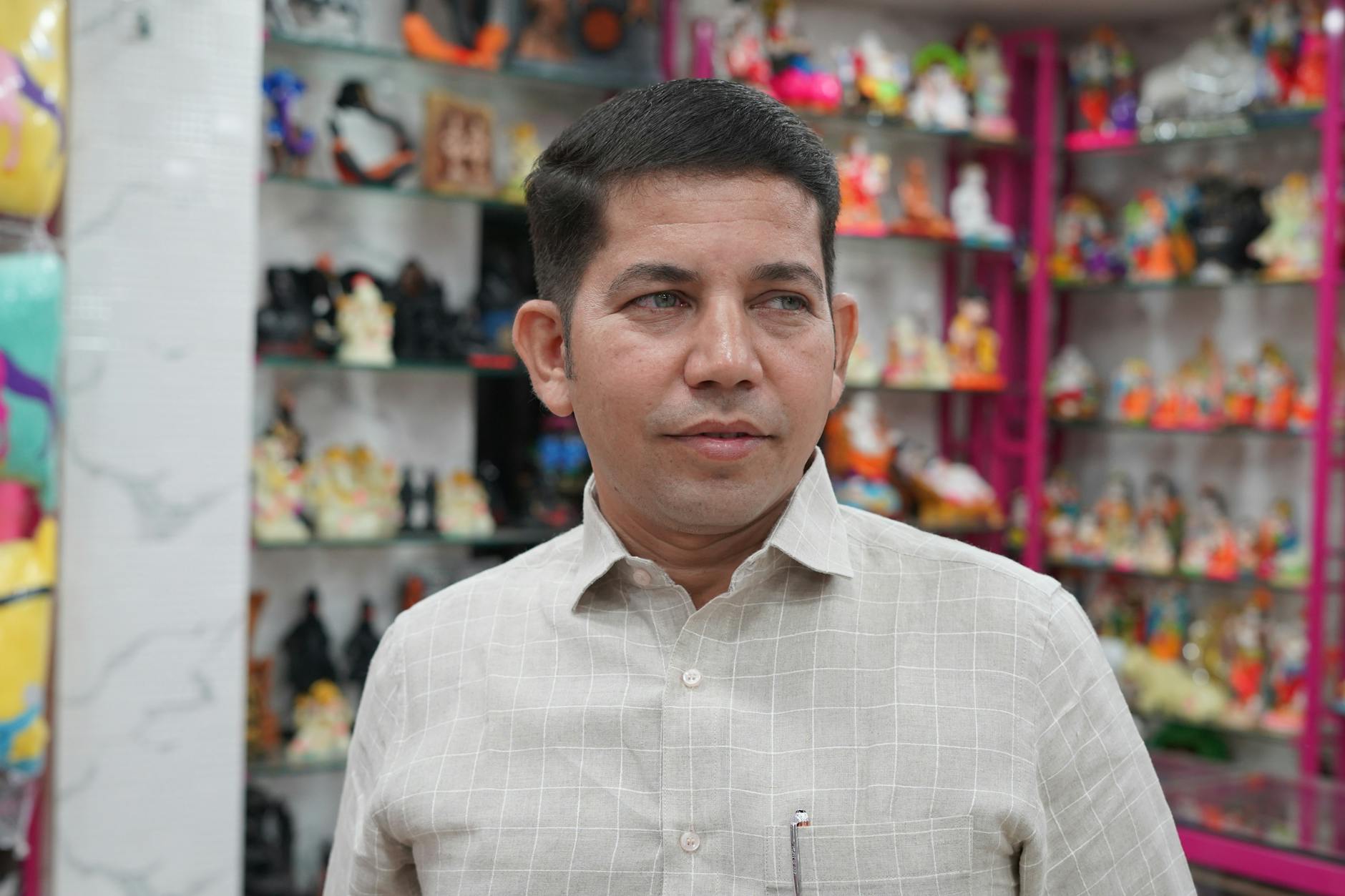 Adult man posing in a toy shop surrounded by colorful decorative figurines.