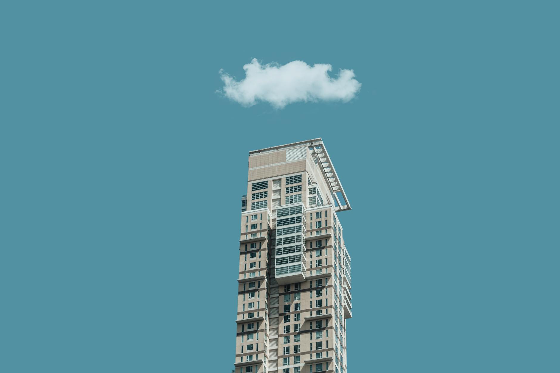 Low-angle shot of a modern high-rise building against a clear sky with a single cloud above.