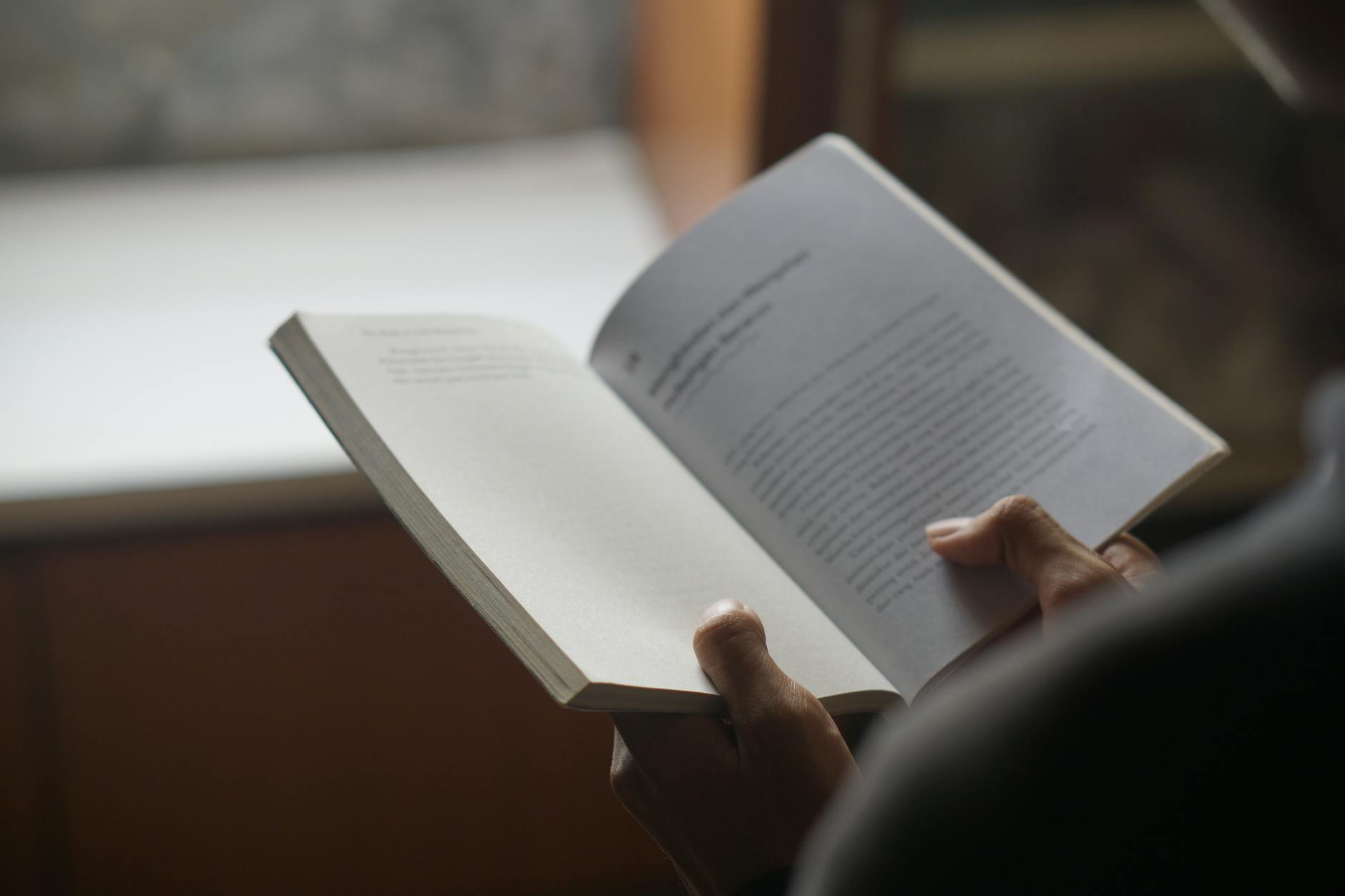 Person reading an open book indoors with a soft focus on the pages, creating a calm study atmosphere.