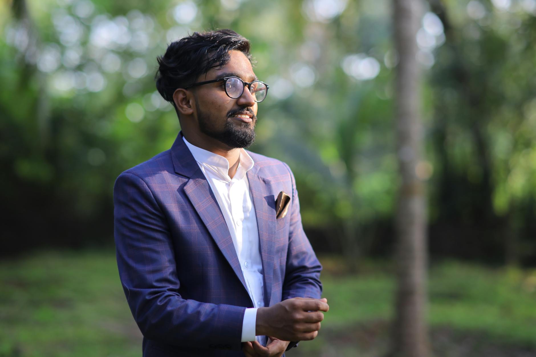 A young man in a suit poses outdoors amidst lush greenery in Kasaragod, India.