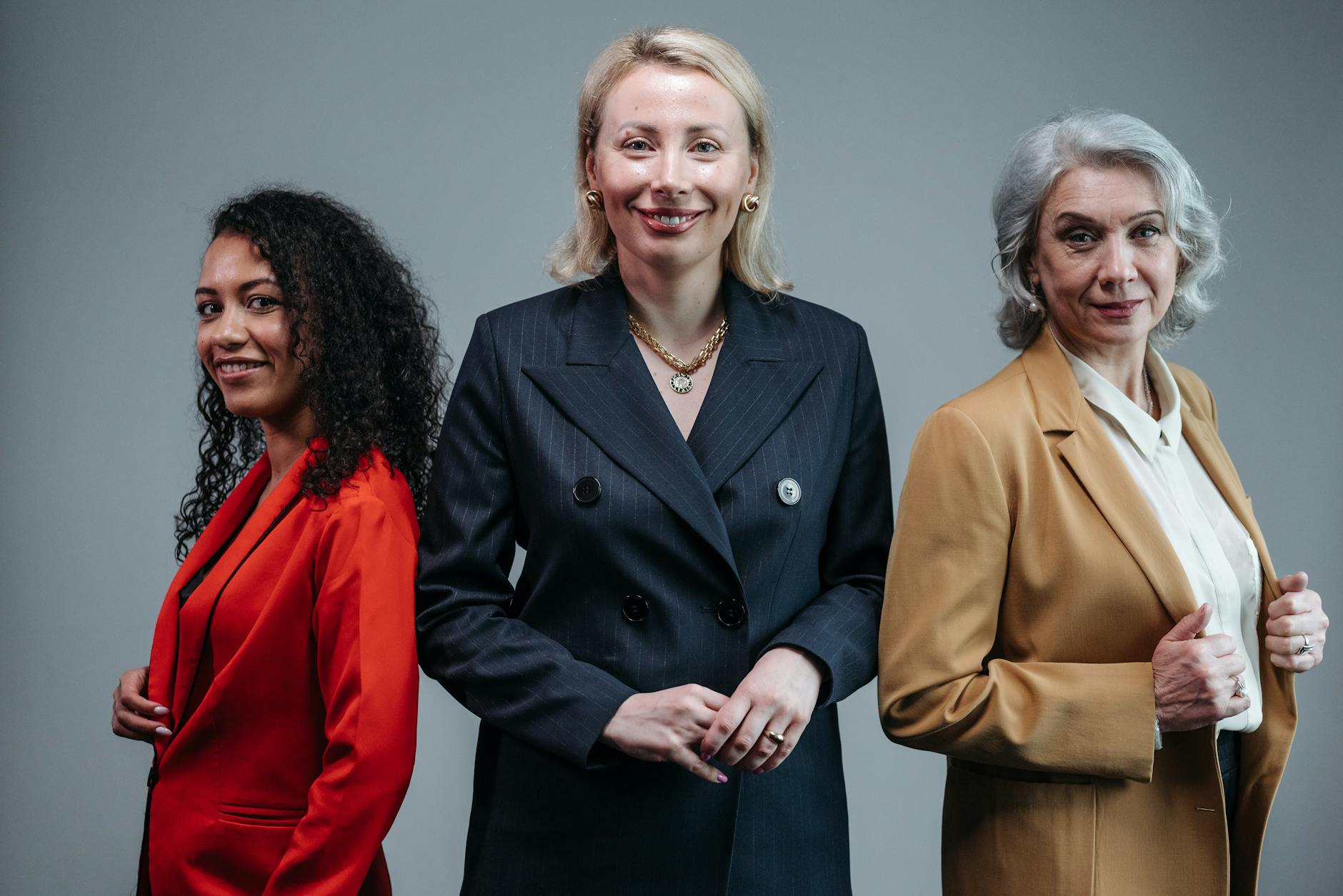 Three confident business women standing in fashionable attire, exuding professionalism.