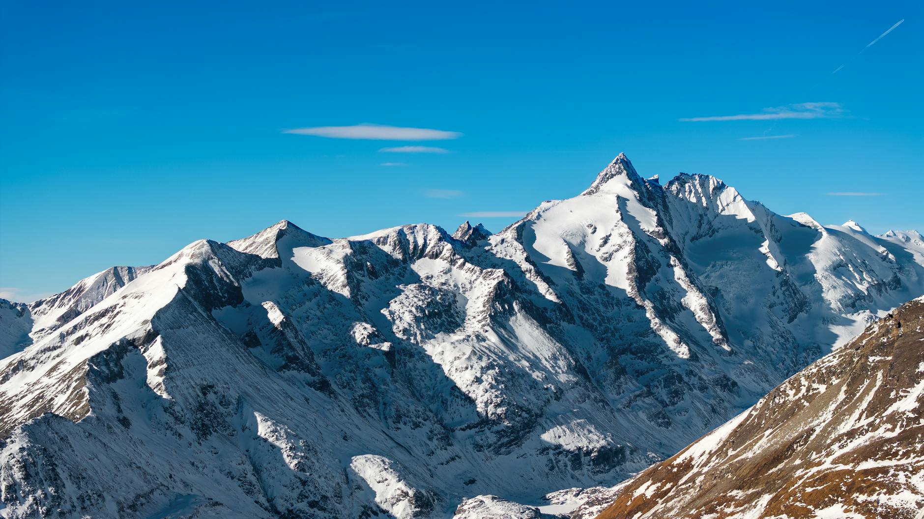 Breathtaking view of snow-covered Alps with clear blue skies, captured at sunrise.