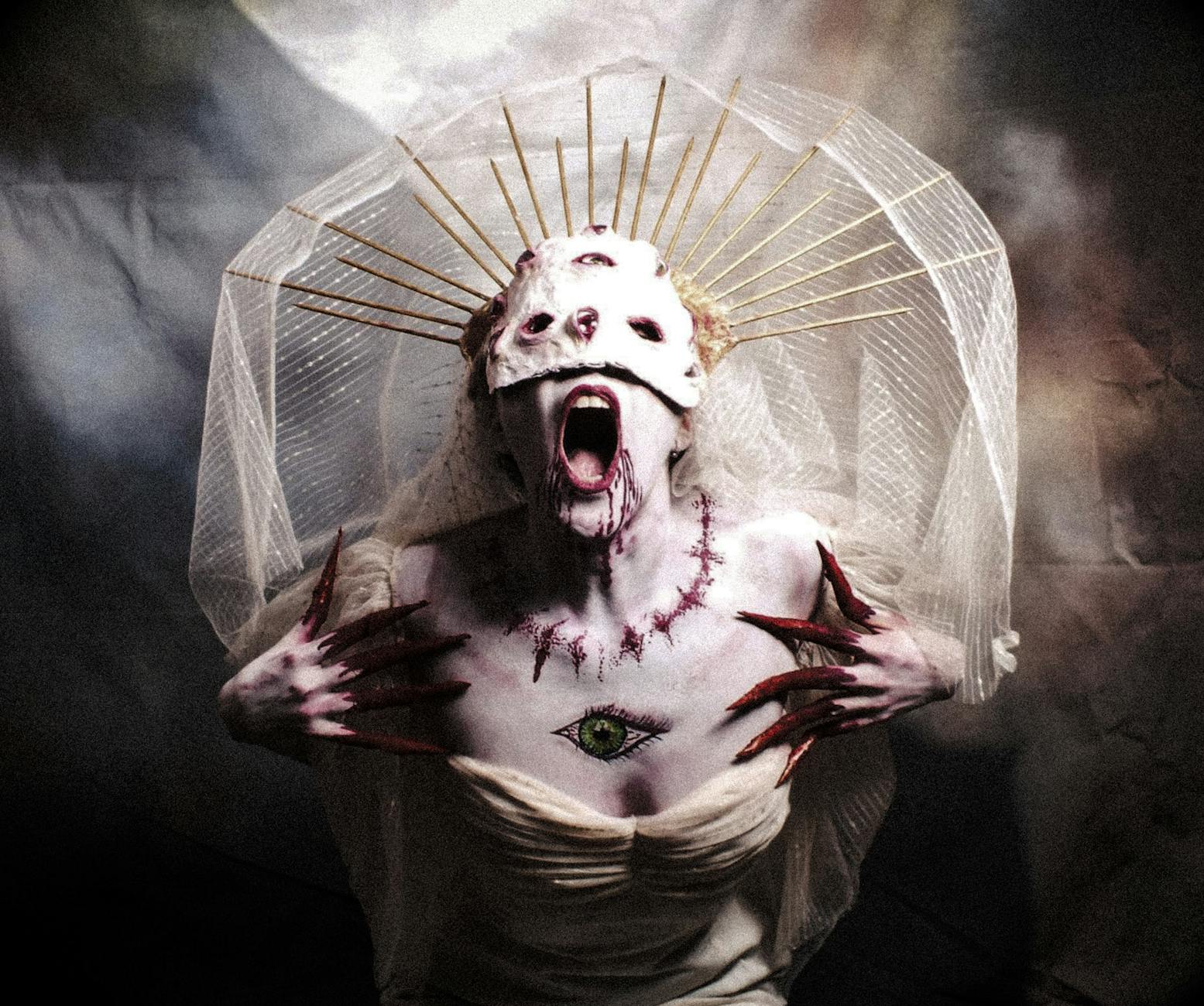 Gothic woman with a haunting costume, veil, and painted mask in an artistic horror portrait.