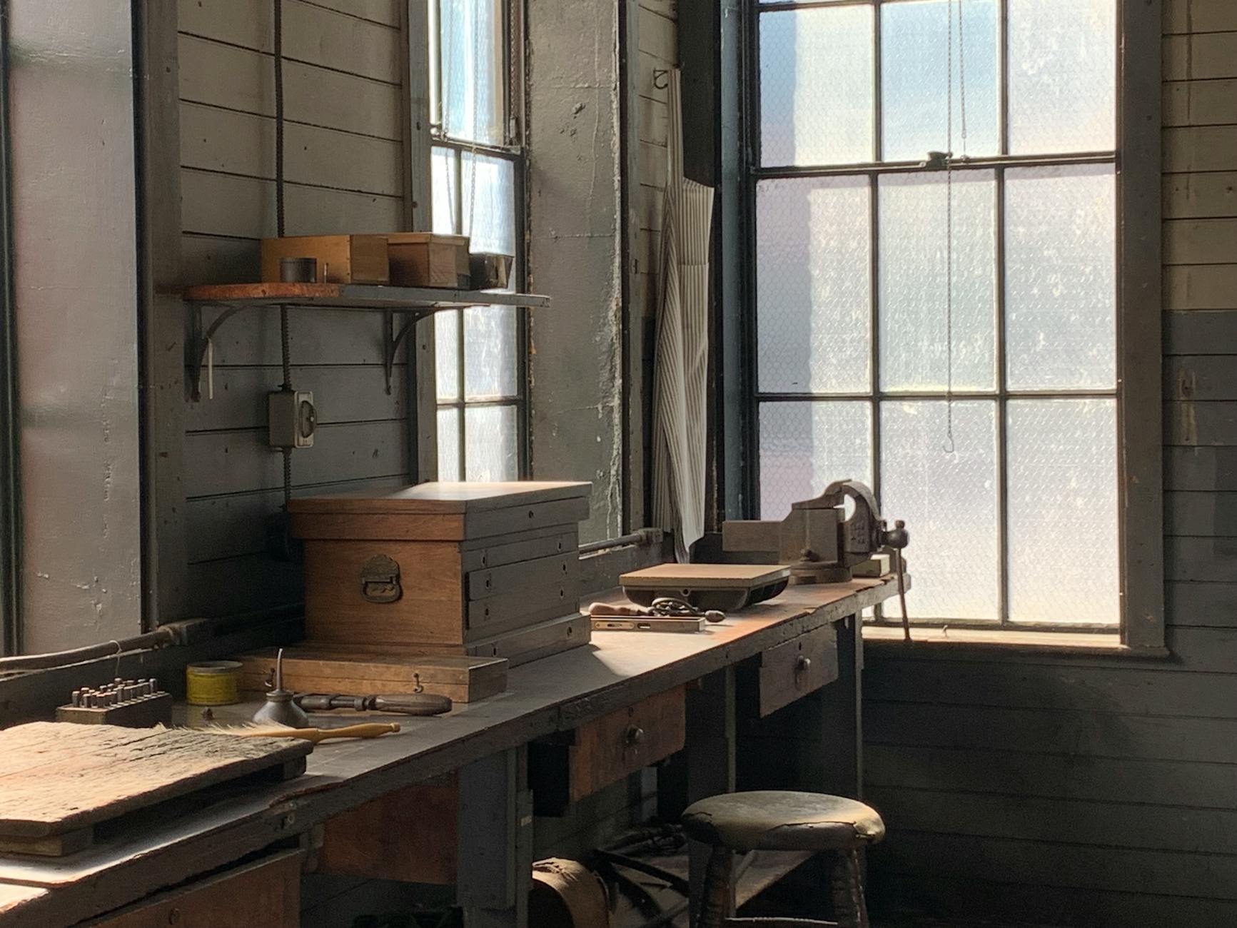 Sunlit historic workshop in New Jersey, showcasing vintage tools and wooden furniture.