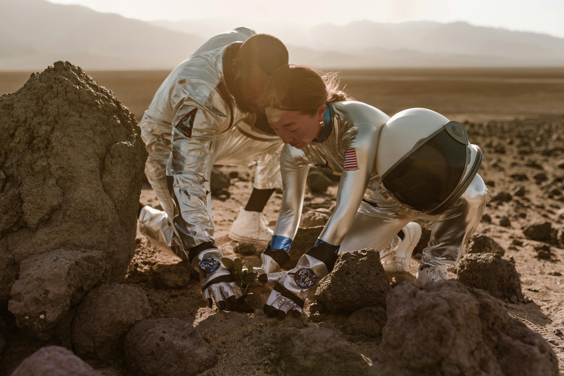 Two astronauts planting a seedling in a rocky desert terrain, symbolizing space colonization.