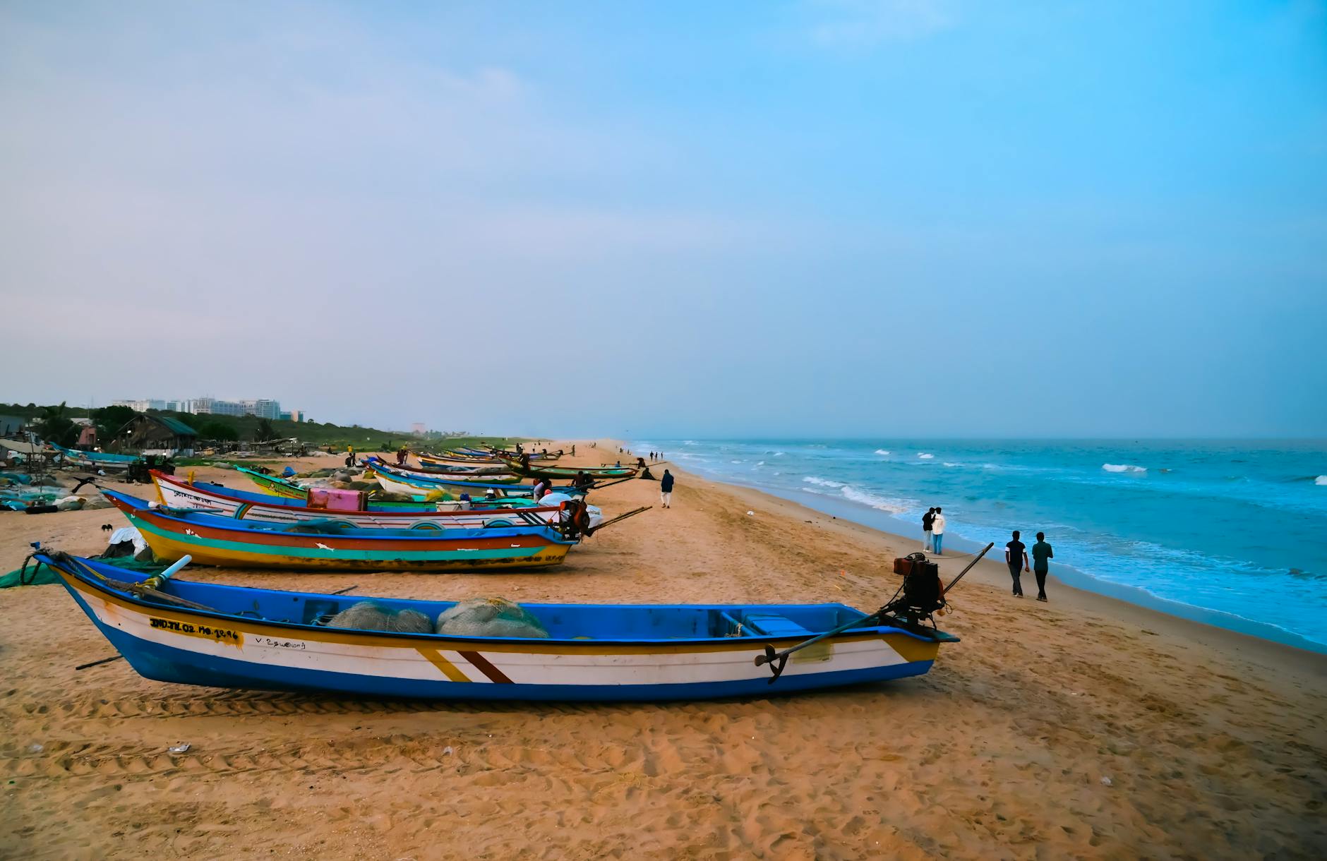 Colorful fishing boats on the sandy beach at sunrise in Chennai, India.