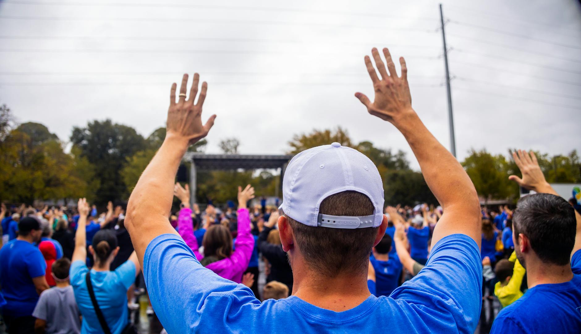 A vibrant crowd raising hands in unison at an outdoor event with people of all ages participating.
