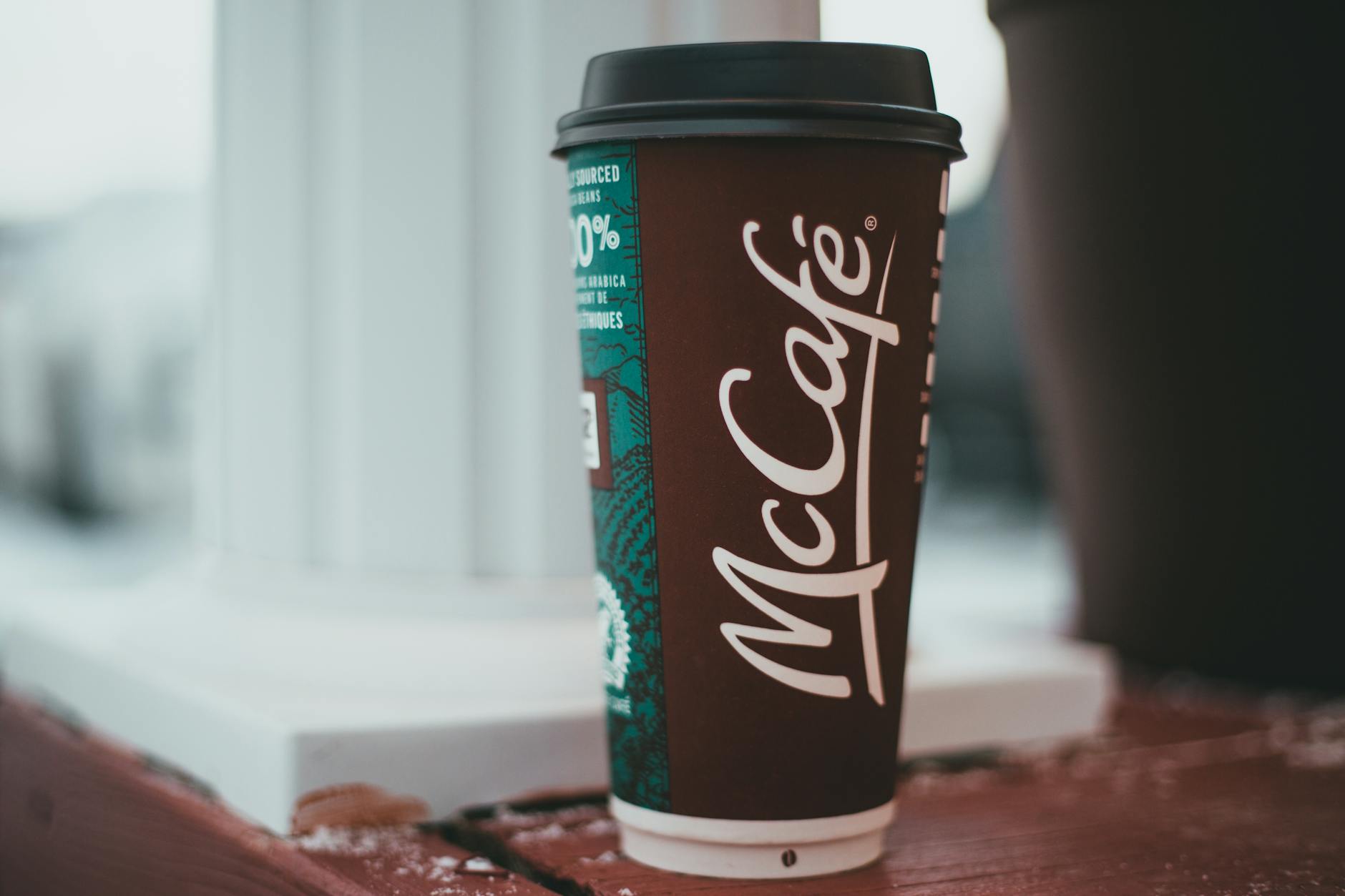 A paper coffee cup with a logo on a table, featuring a blurry background for depth.