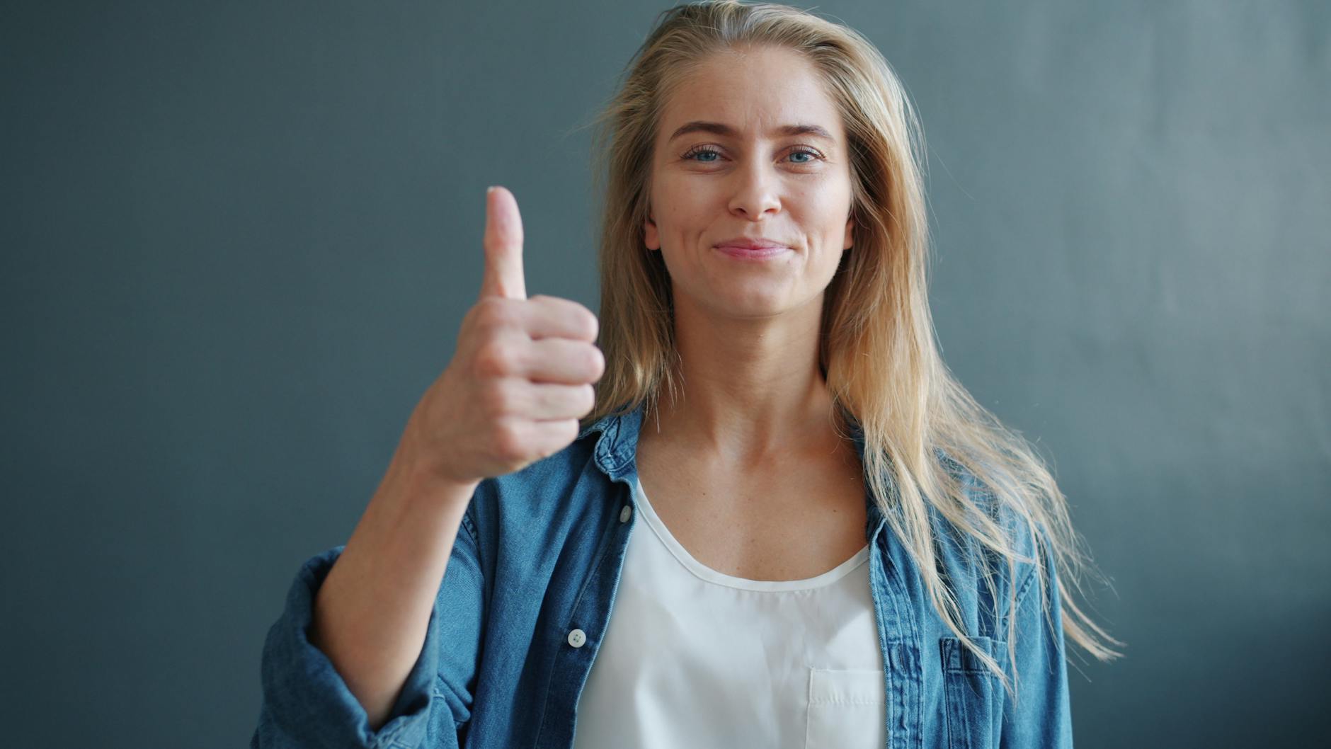 Portrait of a smiling woman giving a thumbs up against a neutral background.
