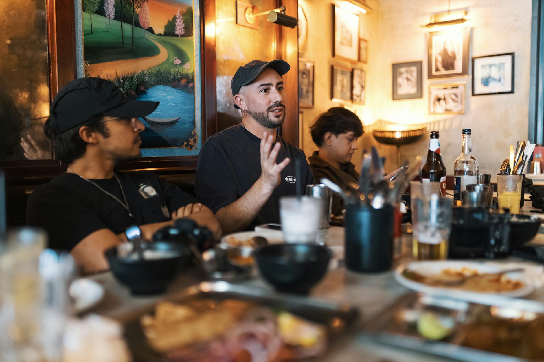A group of adults in casual conversation at a restaurant with food and drinks on the table.