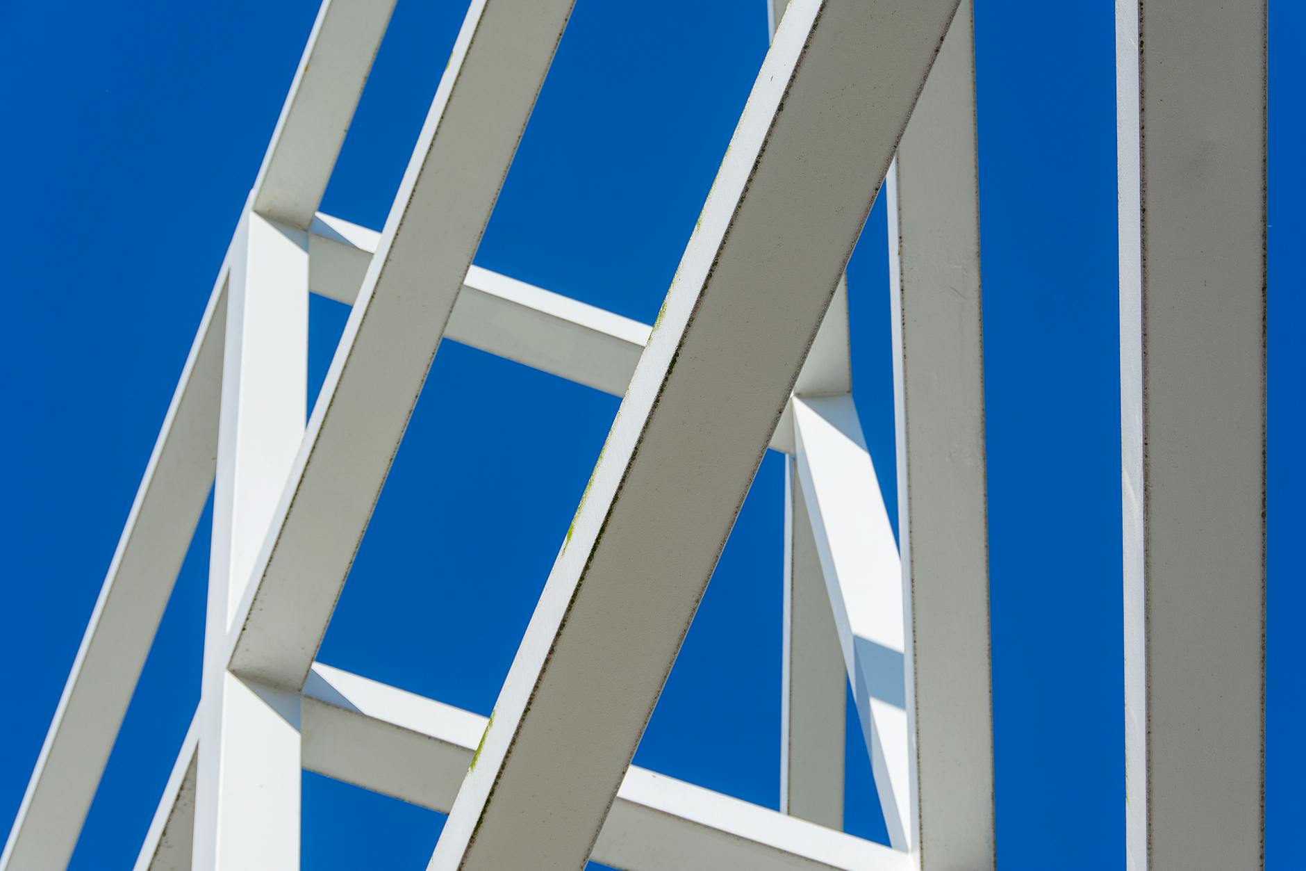 Low angle view of modern white beams forming abstract patterns against a bright blue sky.