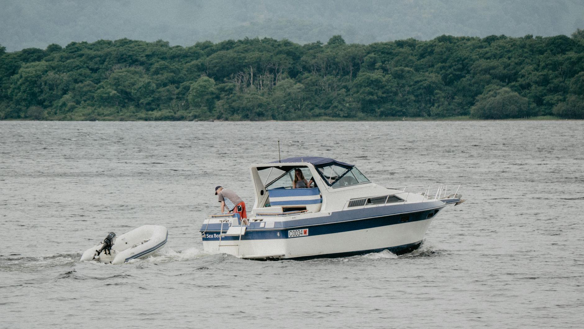 A yacht with passengers sails on a serene lake, surrounded by lush greenery.