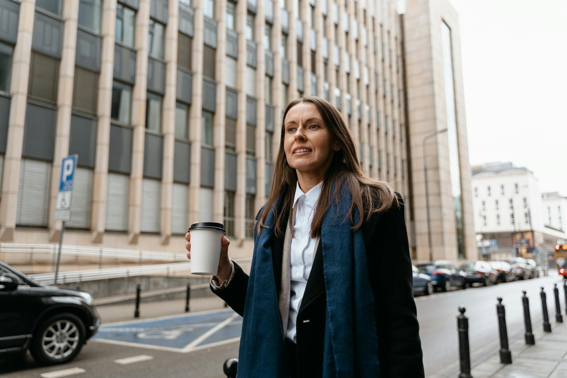 Confident woman holding coffee cup while walking in urban setting on a busy day.