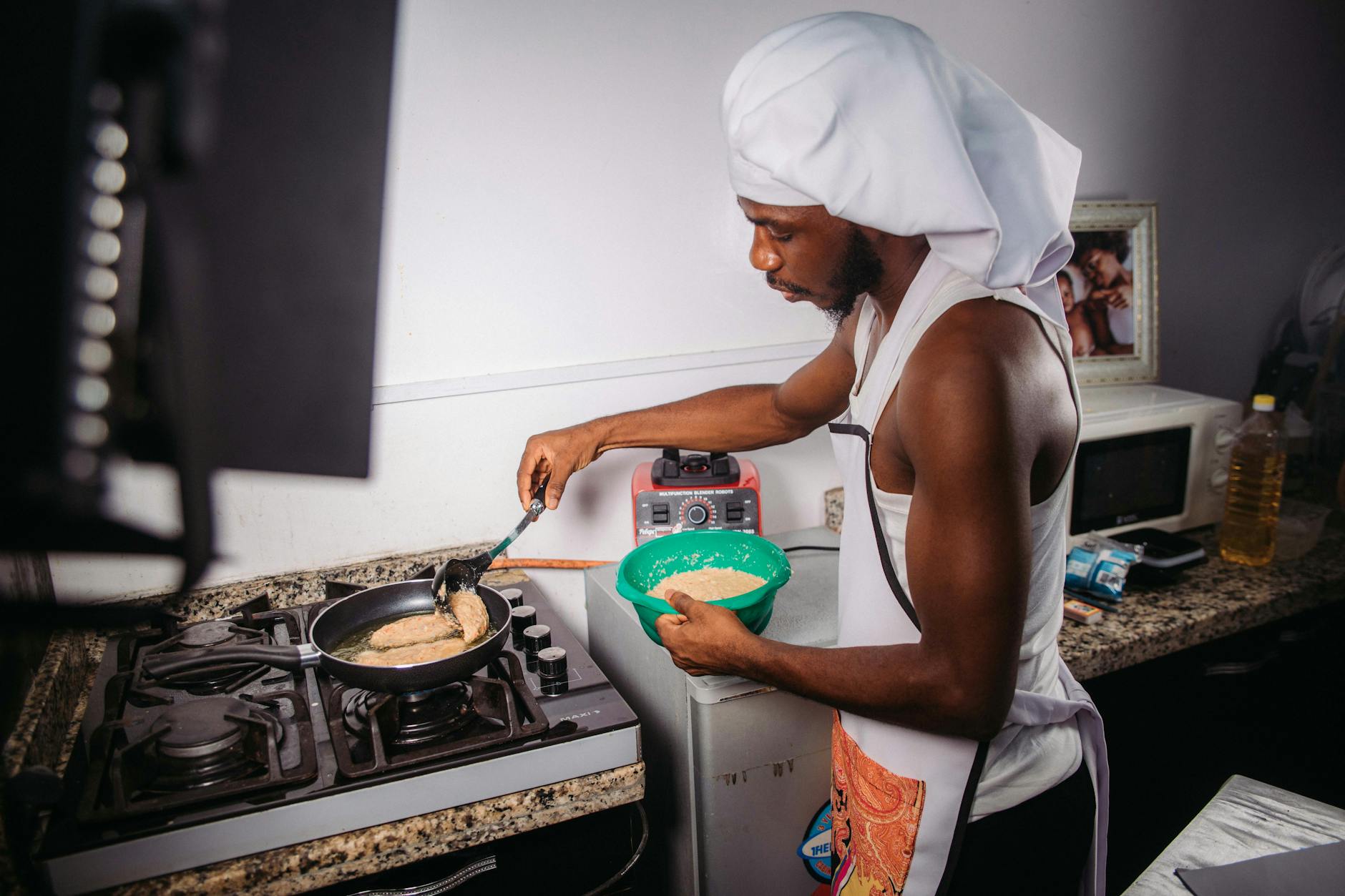A man in a white hat cooking in a kitchen, focusing intently on his task.