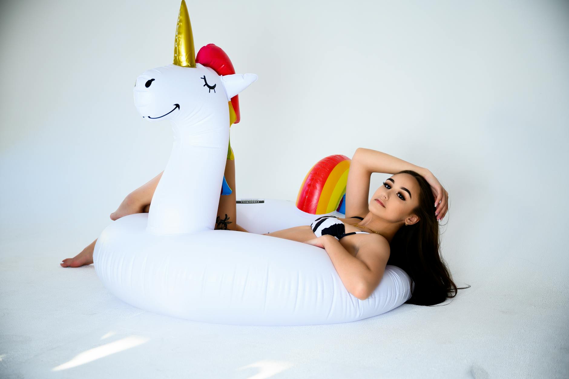 A young woman lounging on a unicorn float during a studio photoshoot, exuding a summer vibe.
