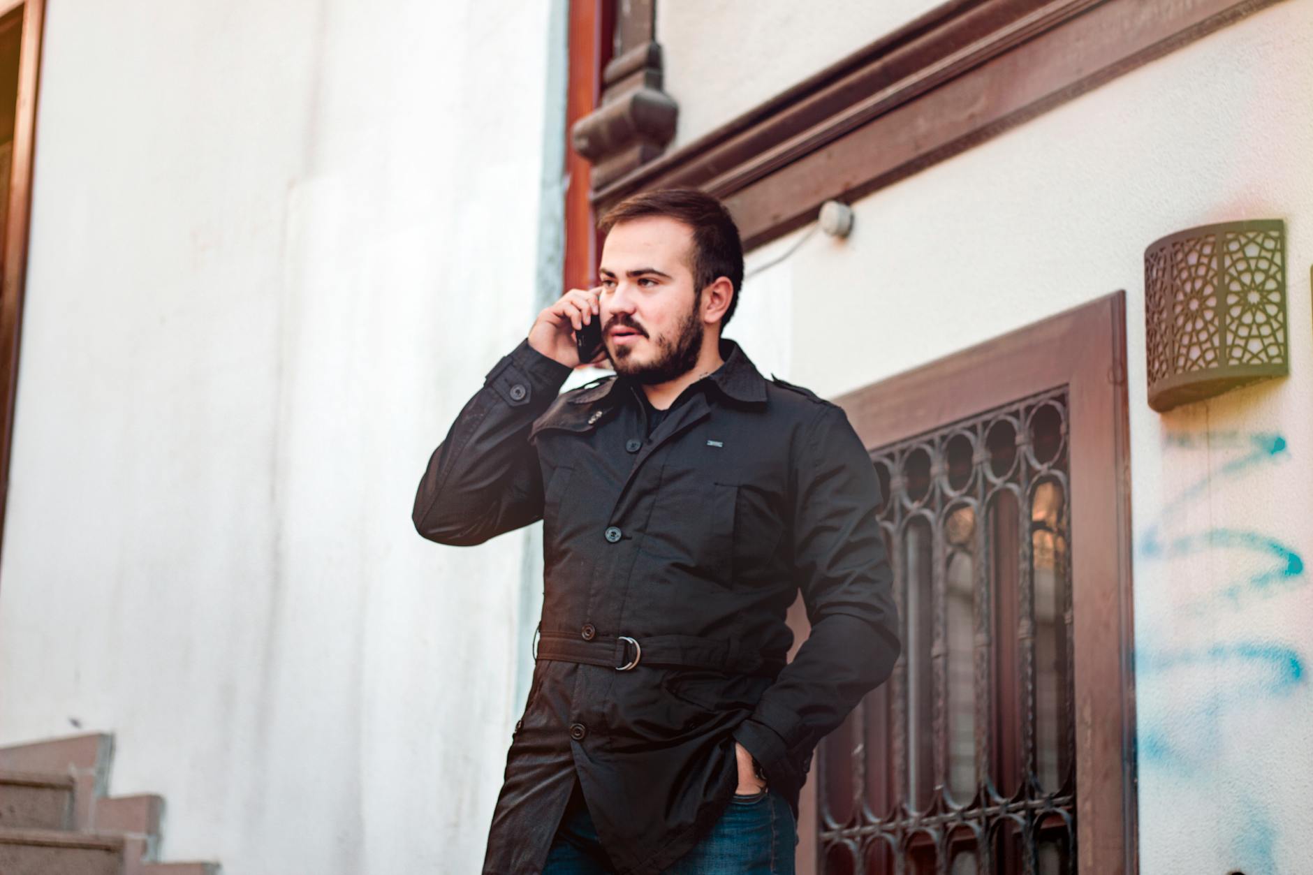 A man in a black jacket stands outdoors in Türkiye, talking on his mobile phone.