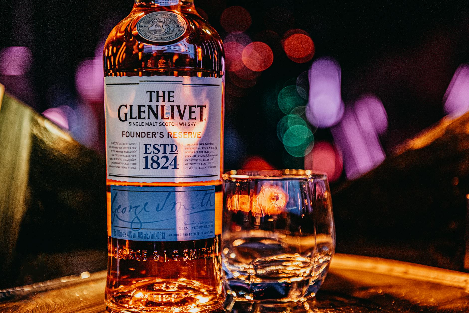A Glenlivet bottle and glass on a tray with colorful bokeh lights in the background.