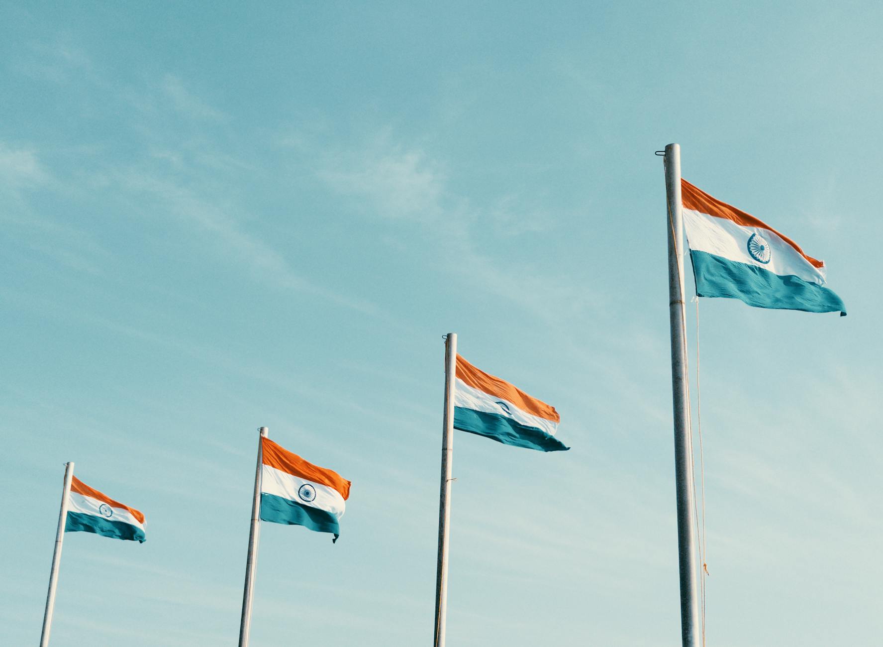 Four Indian flags waving against a clear blue sky, symbolizing patriotism.