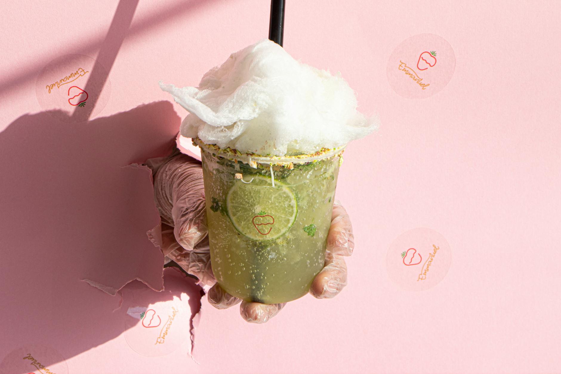 A hand holding a lime drink with cotton candy against a pink wall, symbolizing freshness.