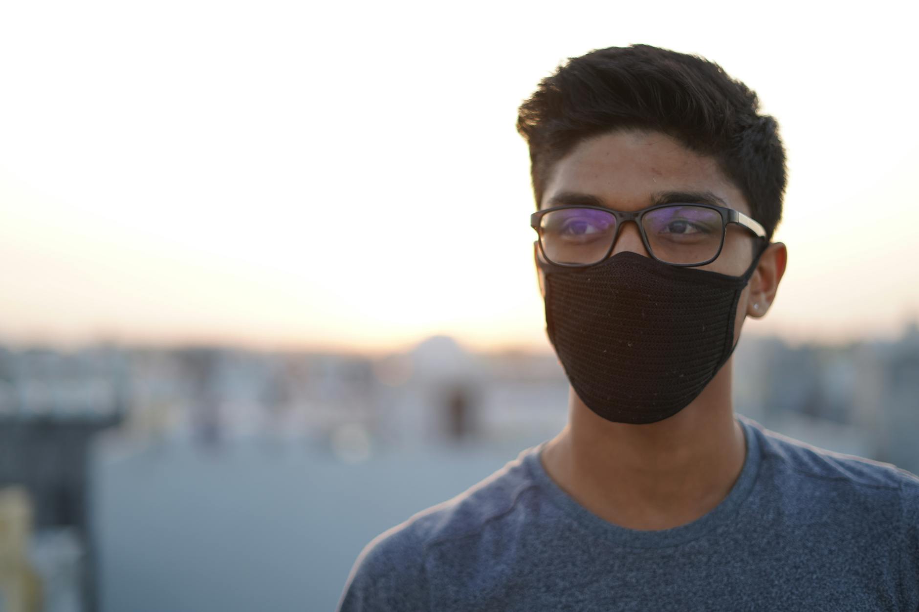 Portrait of a young man wearing eyeglasses and a mask outdoors at sunset, embracing the new normal.
