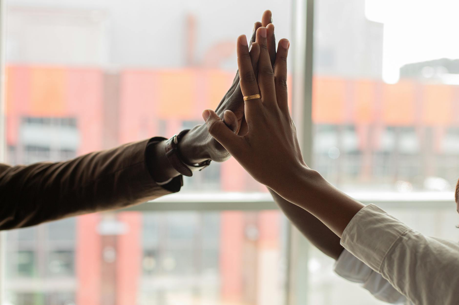 Close-up of a multiracial high five showing teamwork and success. Indoors setting with blurred city background.