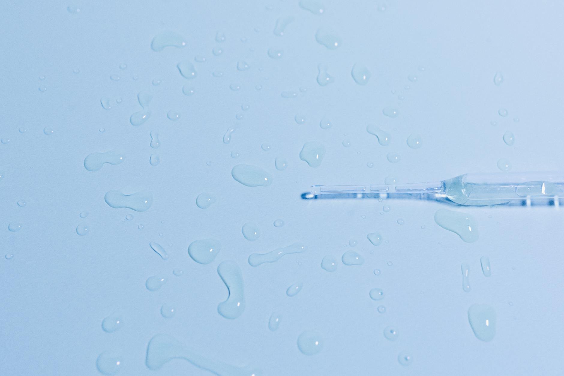 Detailed close-up of a glass pipette on a wet surface with scattered water droplets.
