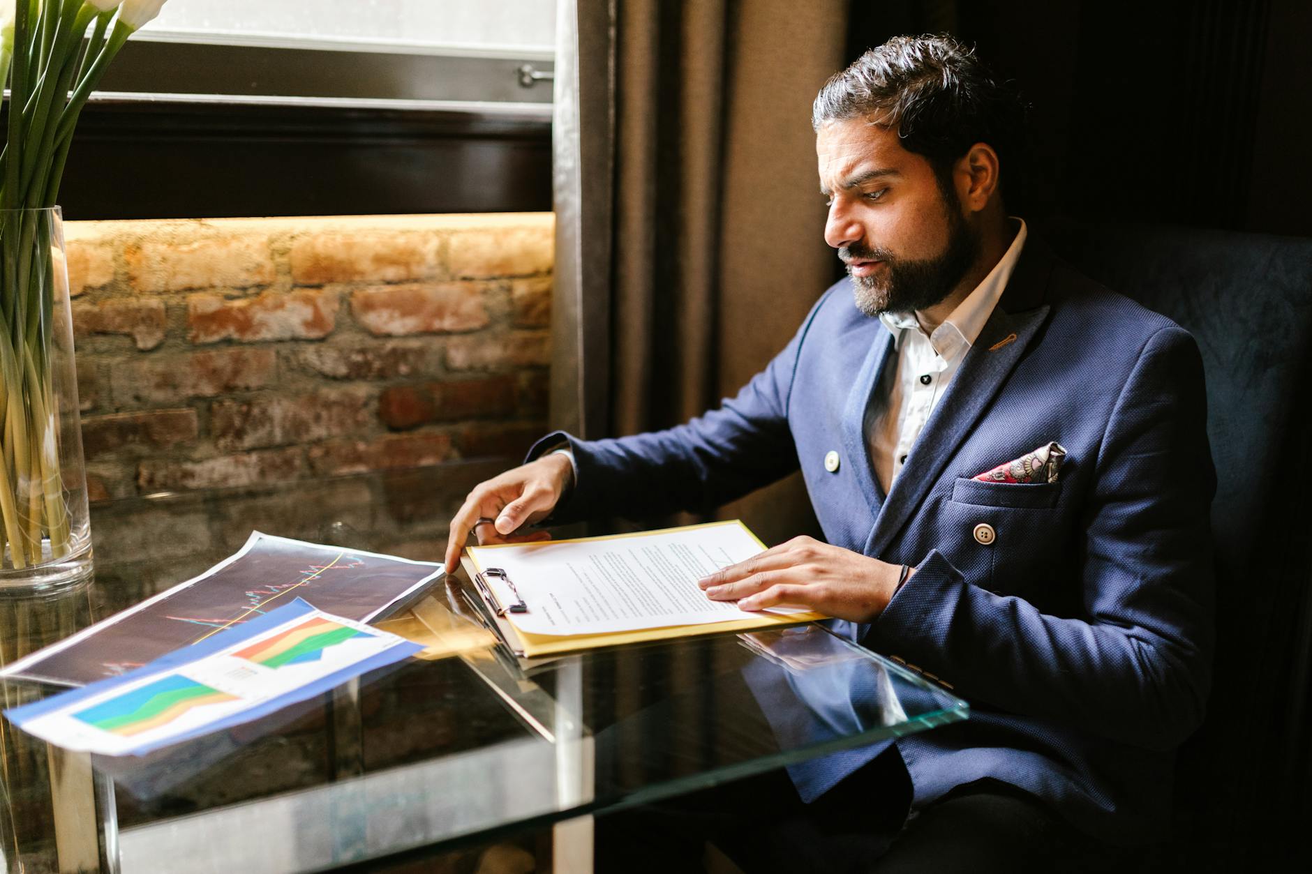 A businessman in a suit reviewing financial documents at a desk in an office setting.