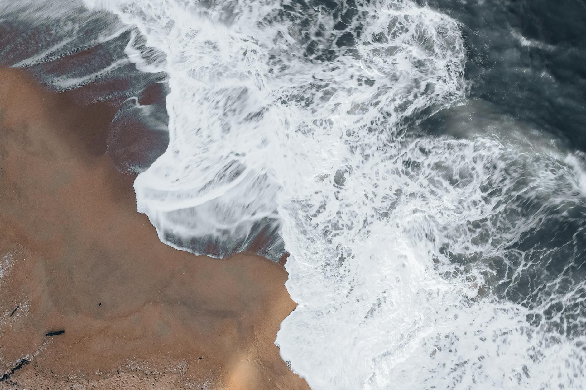 A captivating aerial view of waves crashing on a sandy shore creating a dynamic seascape.