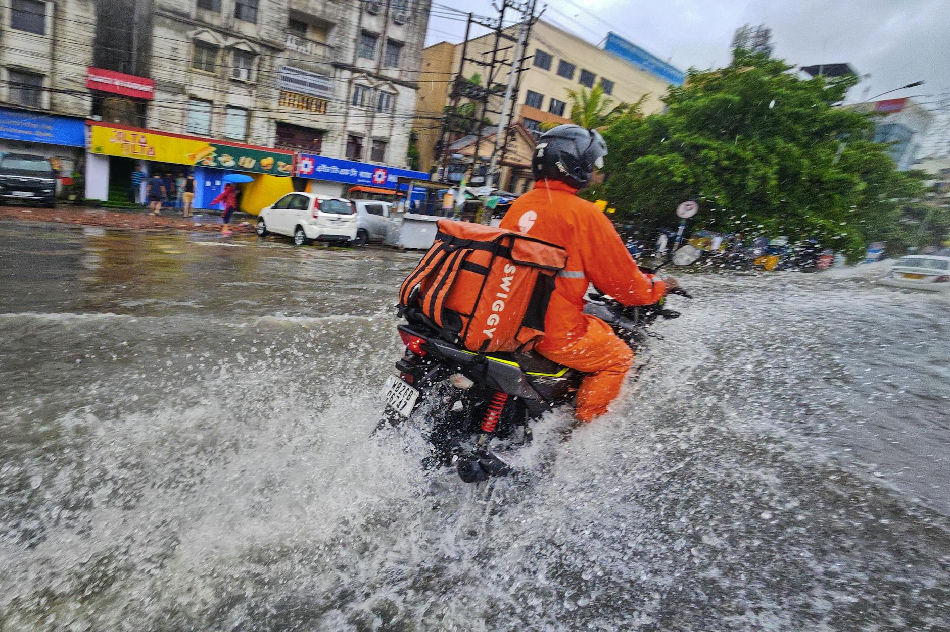 A delivery person on a motorcycle navigates flooded streets of Kolkata, India, during rain.