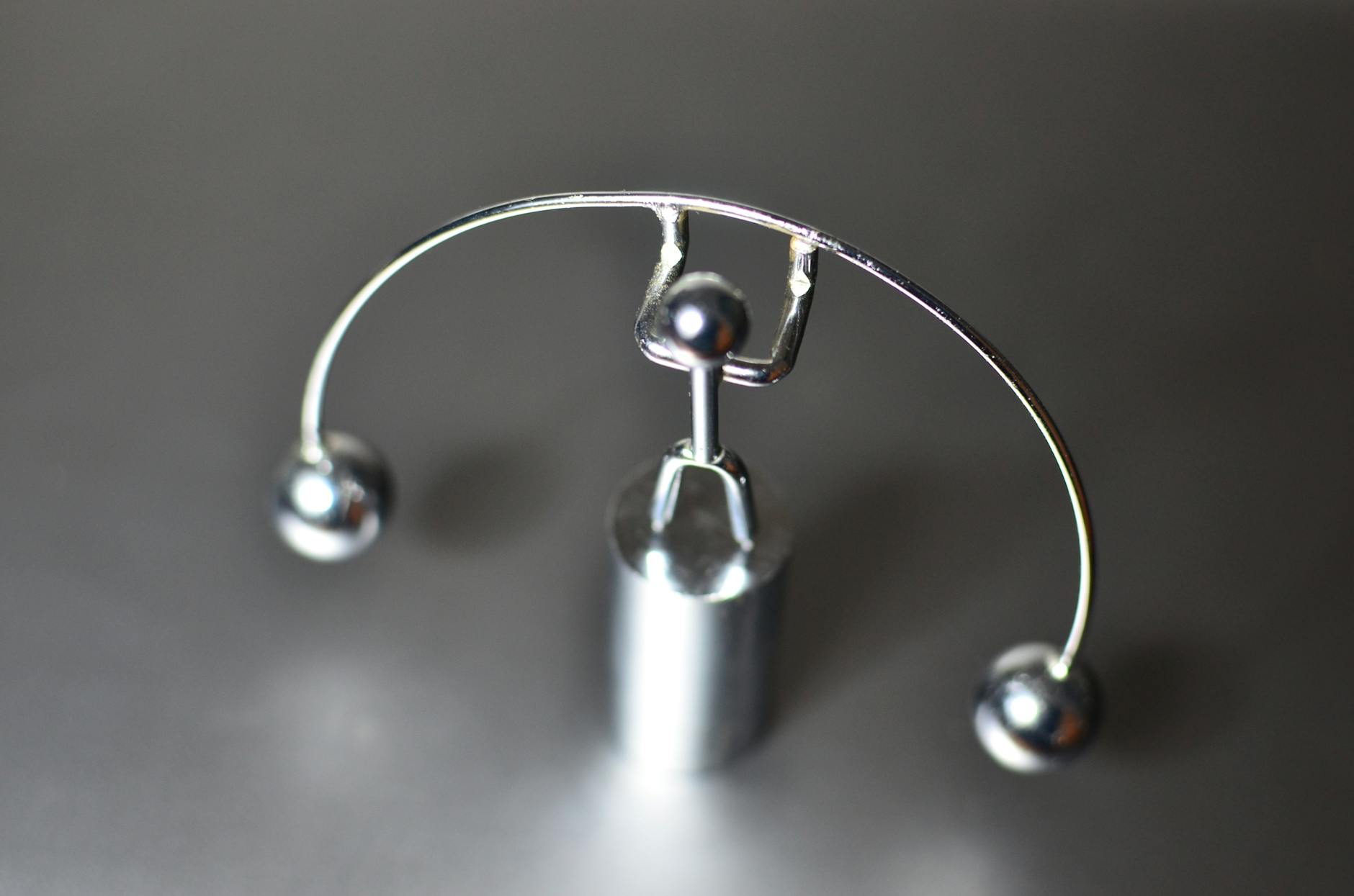Stainless weightlifter kinetic perpetual dynamic motion toy with balance balls placed on gray table in light room on blurred background