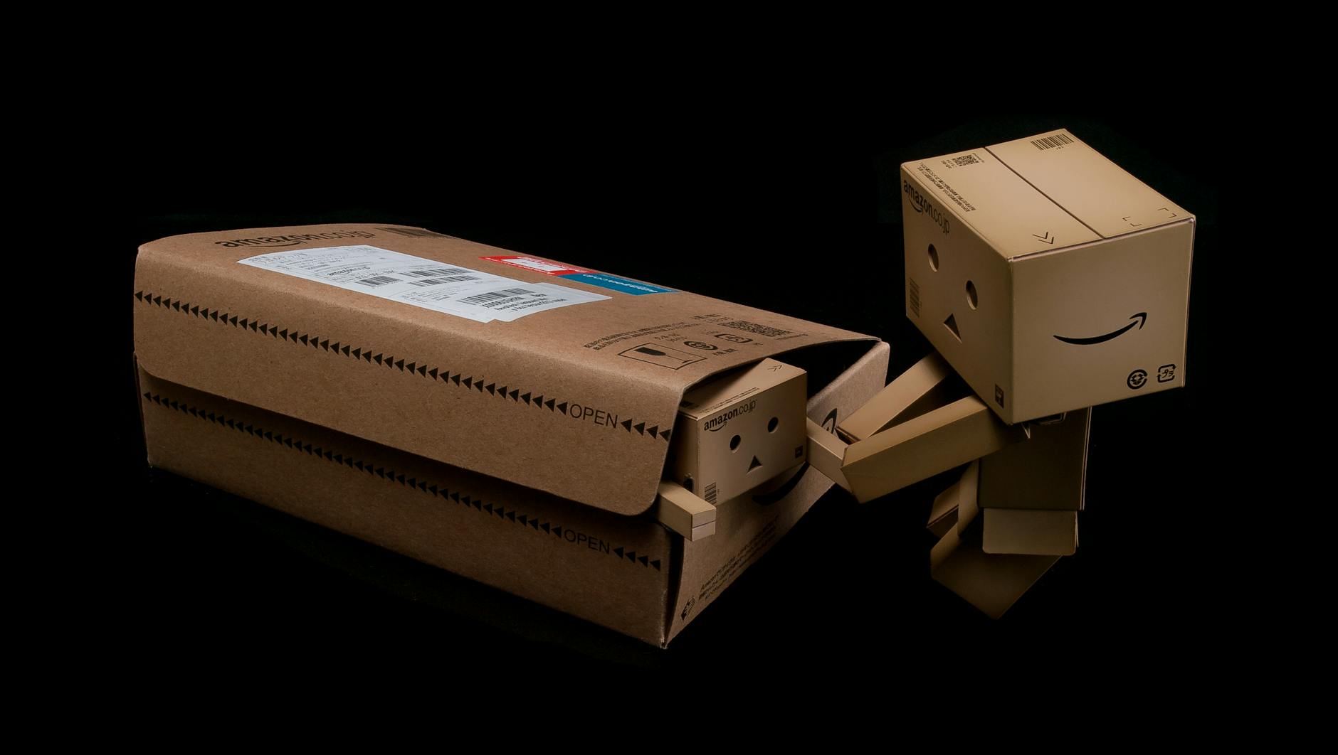 Whimsical cardboard robot figure emerging from a shipping box on a black background.