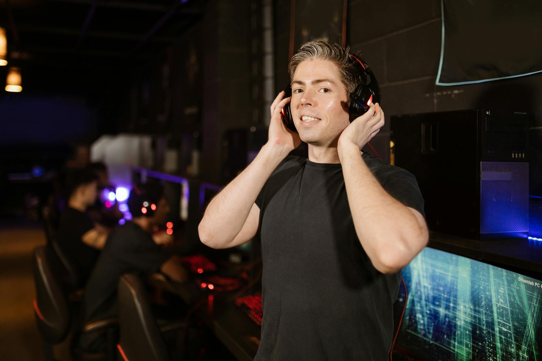 A man in a black shirt with headphones, enjoying gaming in a cyber cafe.