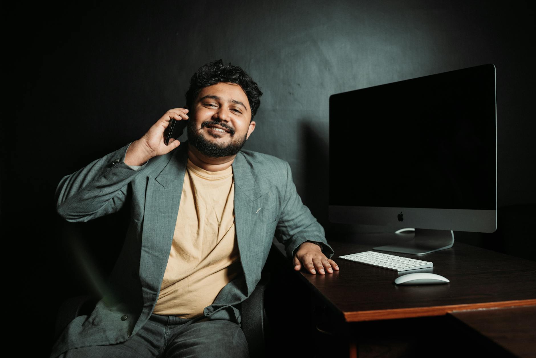 Smiling businessman in a suit talking on the phone at a desk with a computer.