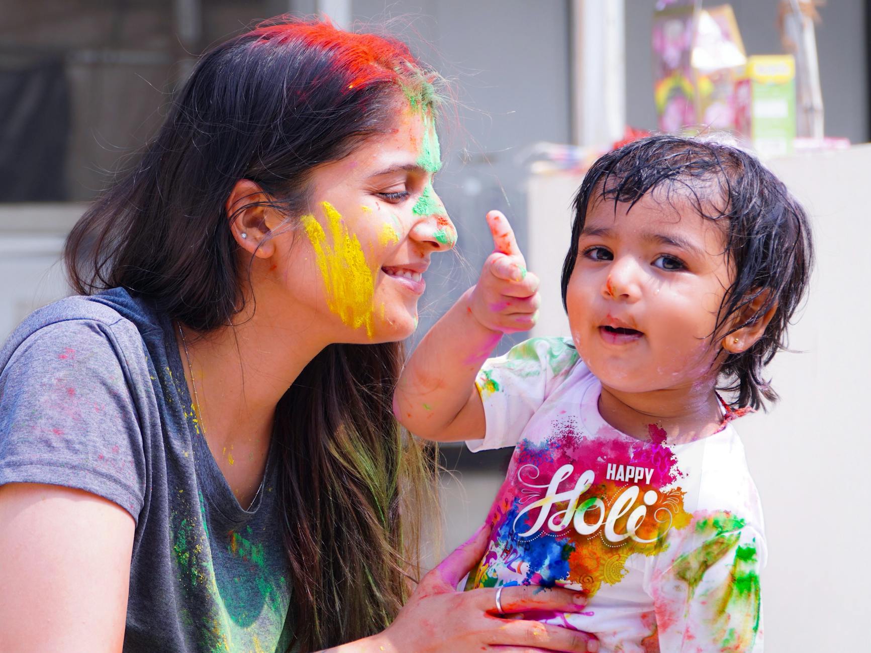 Woman and child enjoying vibrant Holi festival filled with colorful powders.