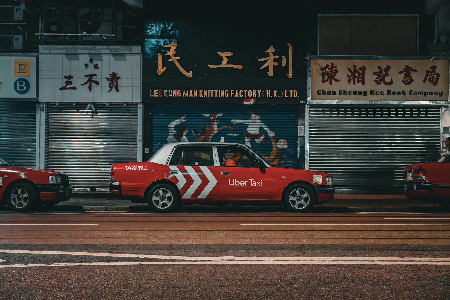 Red Uber Taxi parked on a vibrant Hong Kong city street at night.