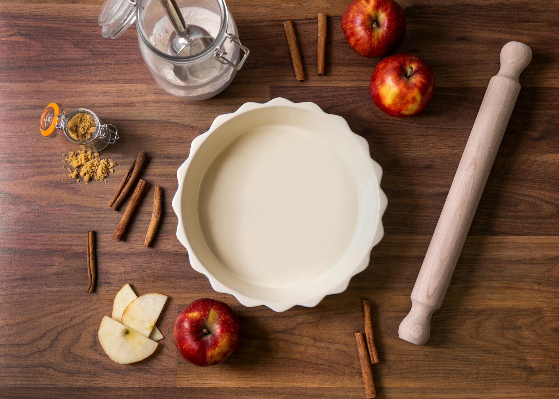 Overhead view of ingredients for apple pie, including apples, cinnamon sticks, and rolling pin.
