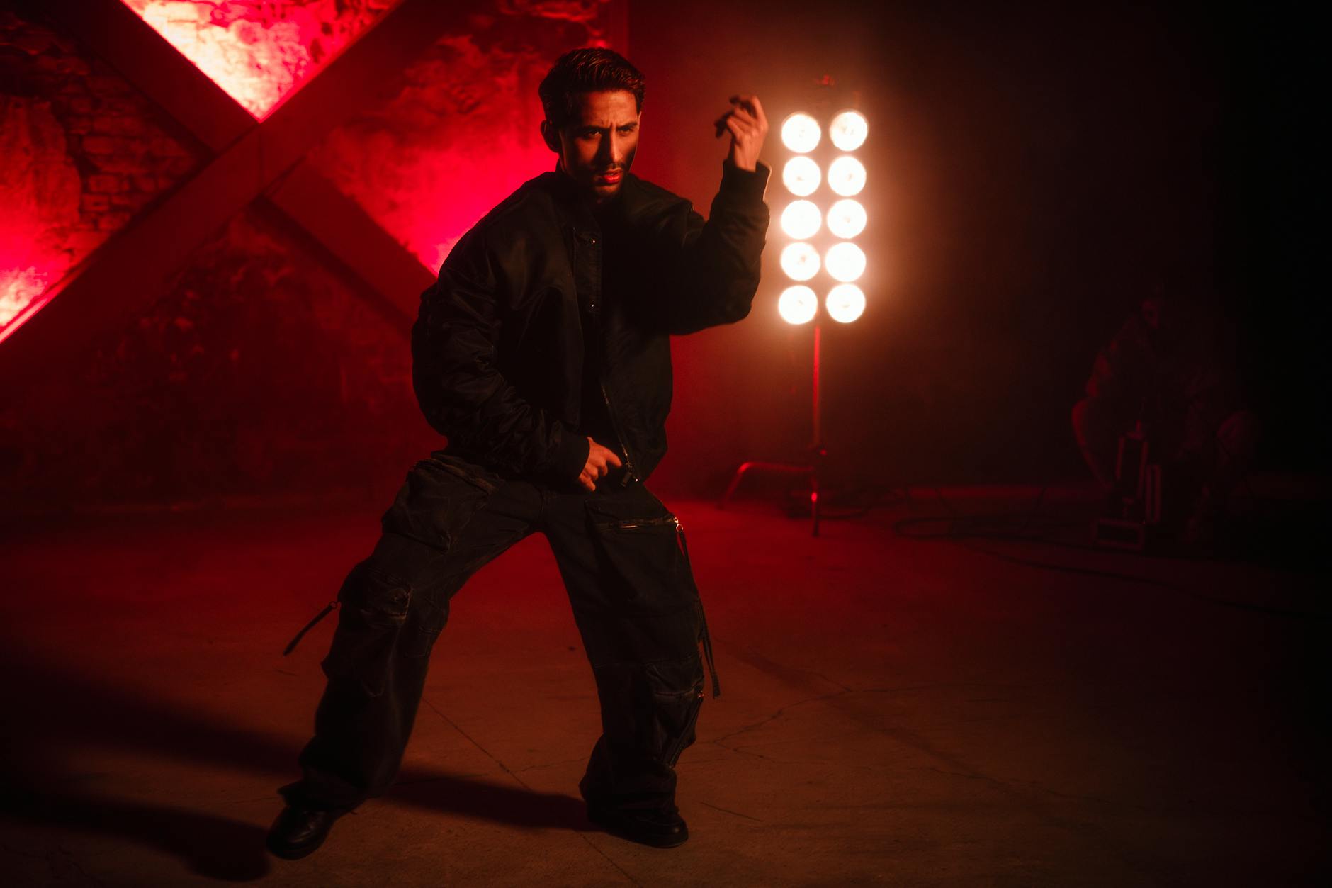 Man in dark clothing poses under dramatic red lighting, creating artistic ambience.