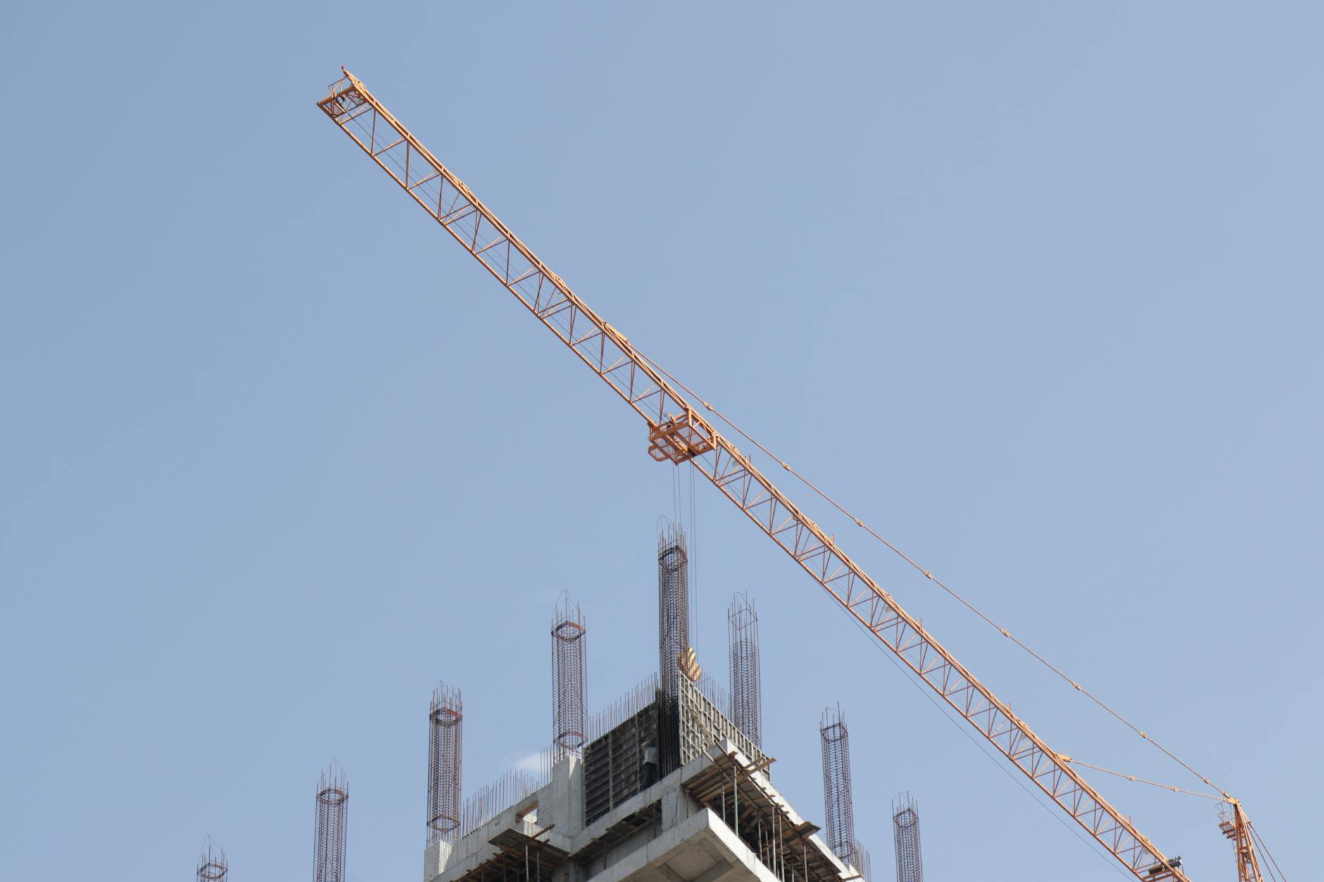 Tower crane working on a high-rise building construction site against a clear blue sky.