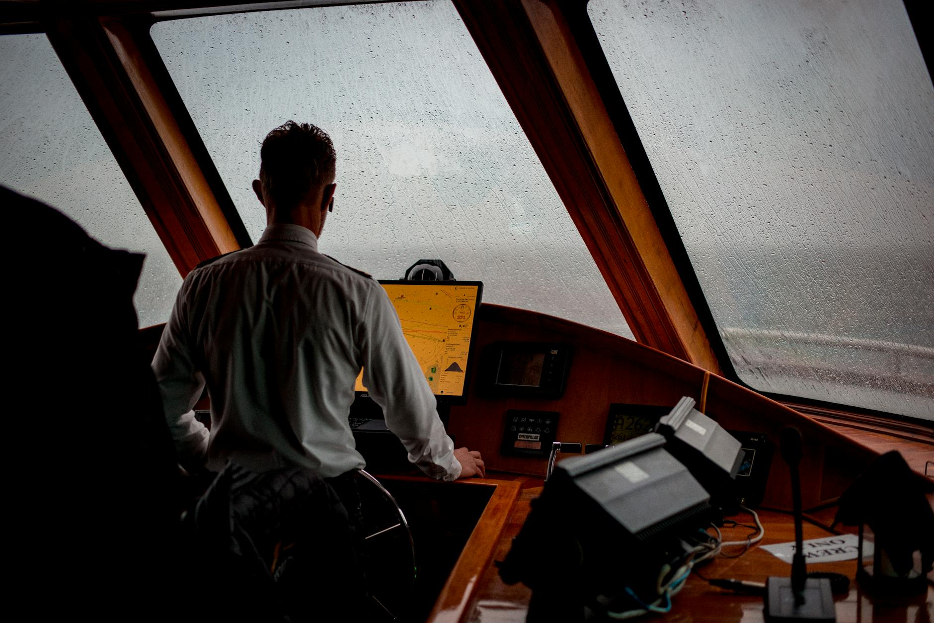 A person navigates a ship's cockpit in rainy weather, focusing on sea travel and transportation.