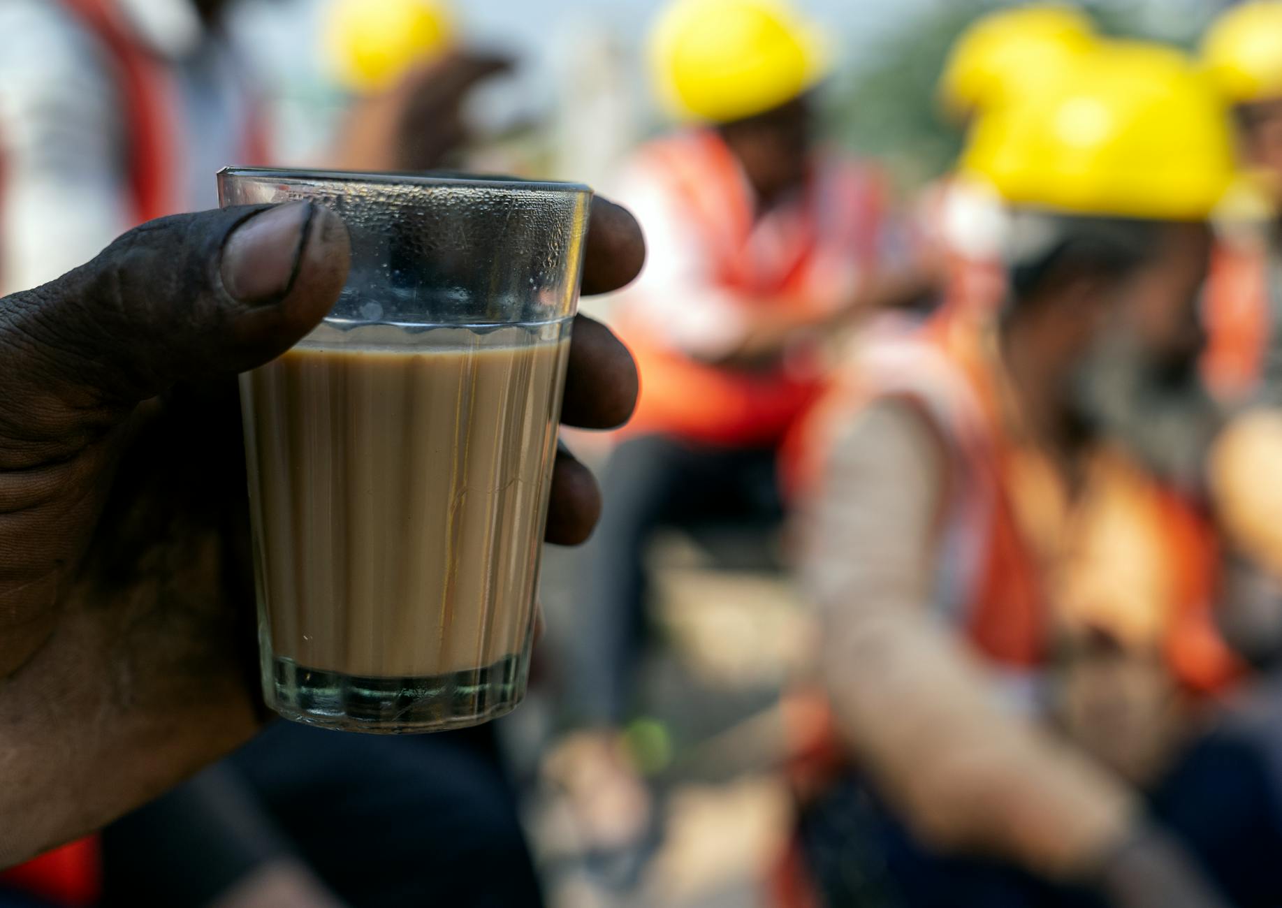 Close-up of construction workers enjoying tea break wearing safety helmets outdoors.