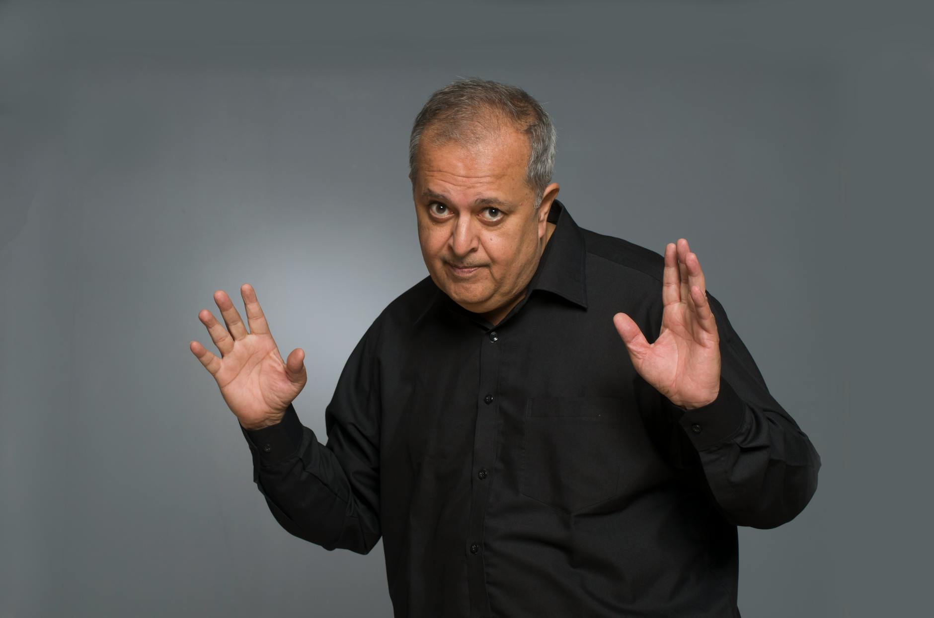 Studio portrait of an older man with a playful gesture in a black shirt.