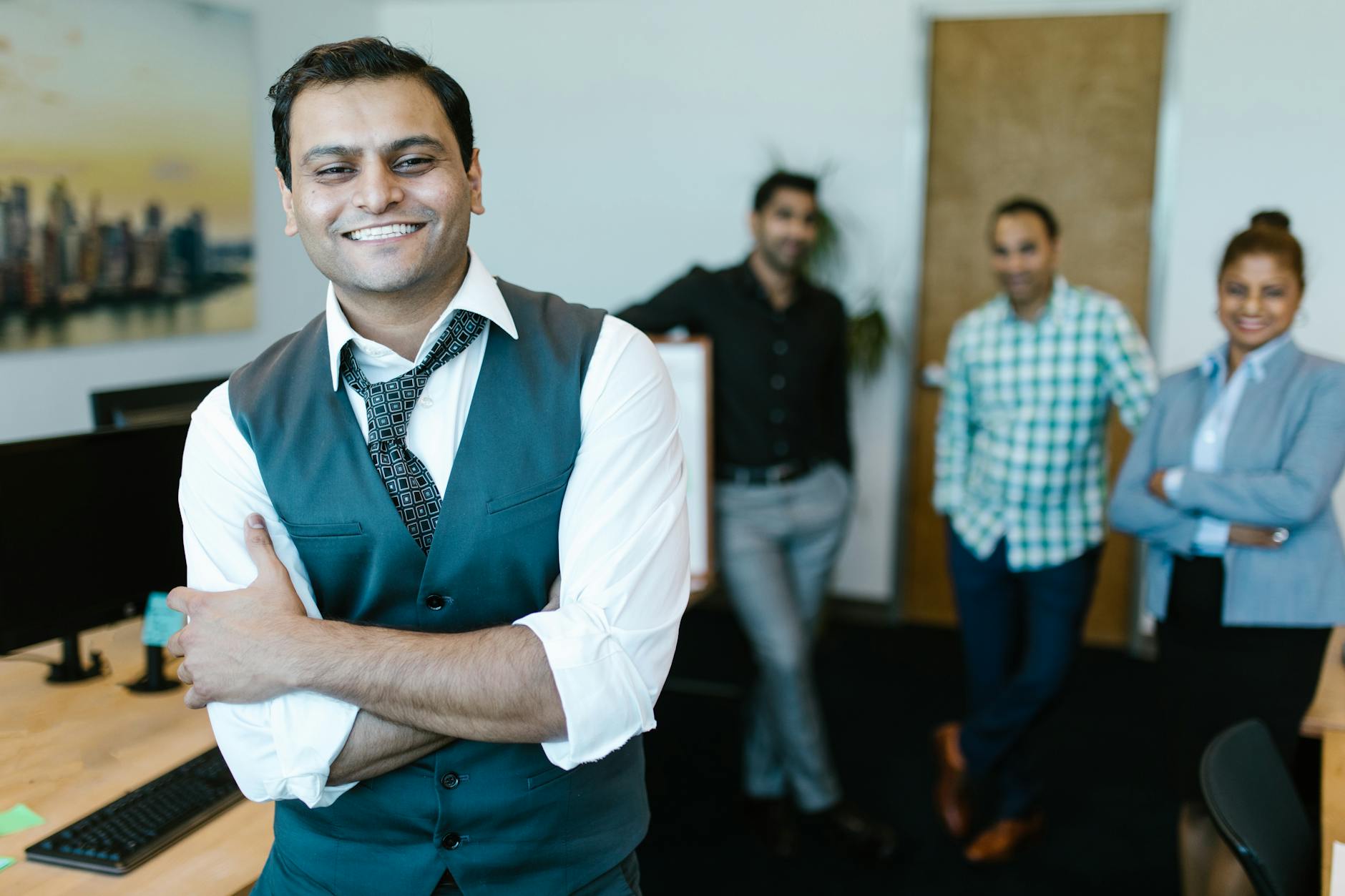 Smiling businessman in a vest with diverse team posing in modern office setting.
