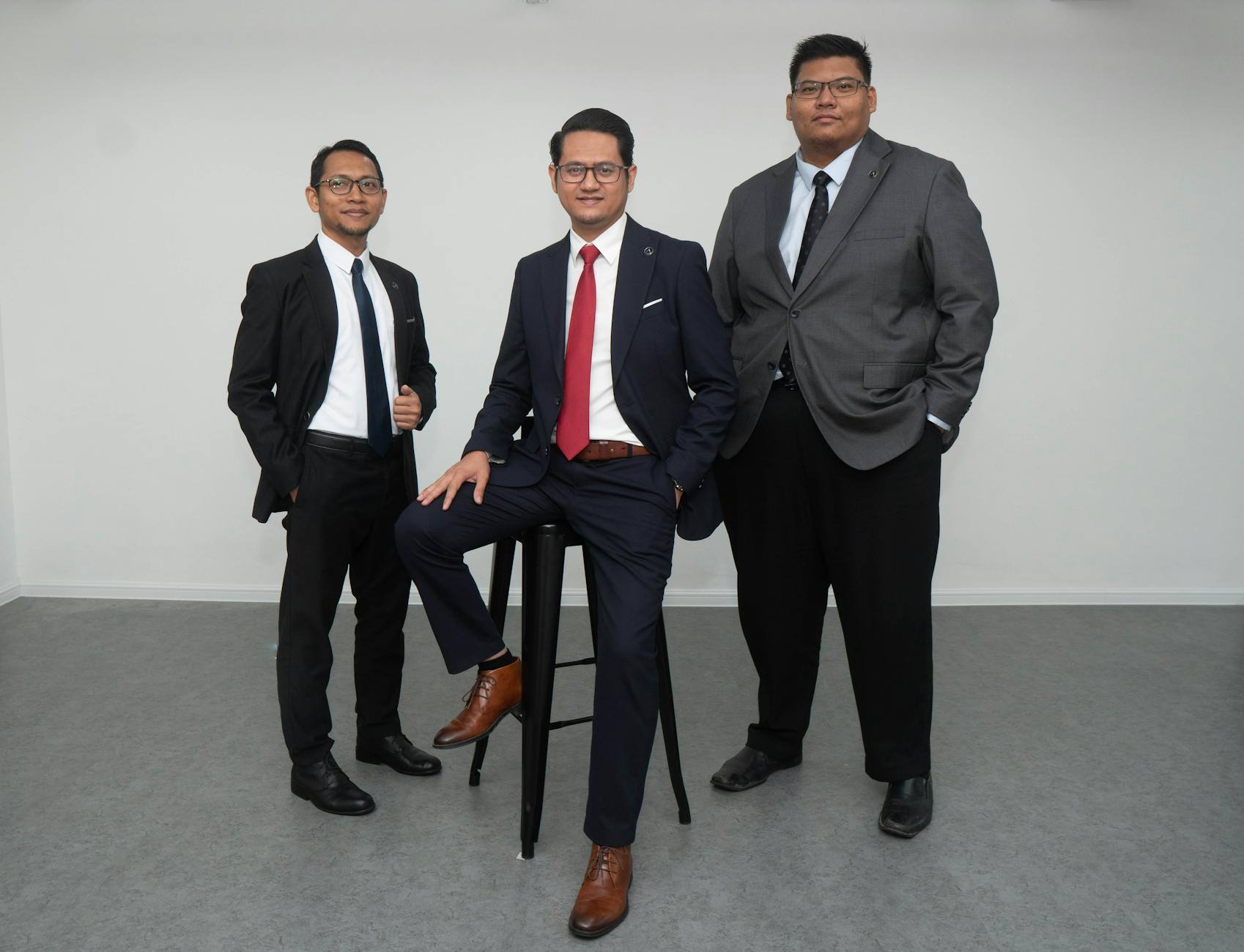 Three confident men in suits posing for a corporate portrait in an indoor setting.