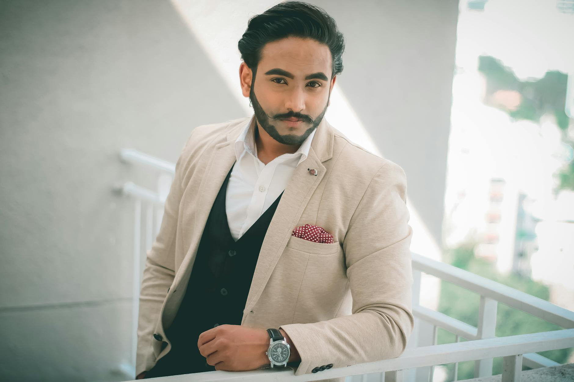 A well-dressed man in elegant formalwear posing confidently on a balcony.
