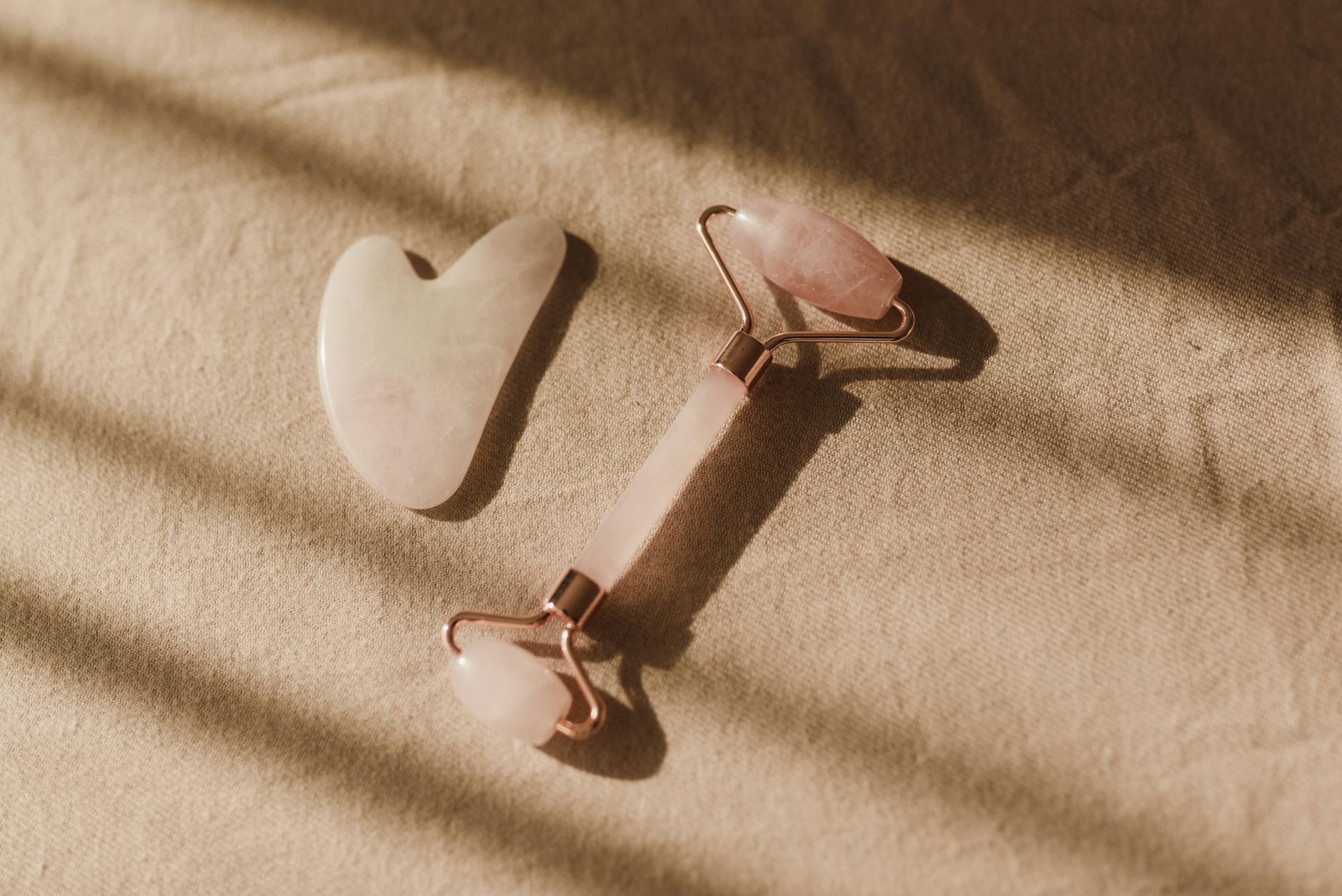Elegant rose quartz facial roller and gua sha laid out on a beige fabric surface with soft lighting.
