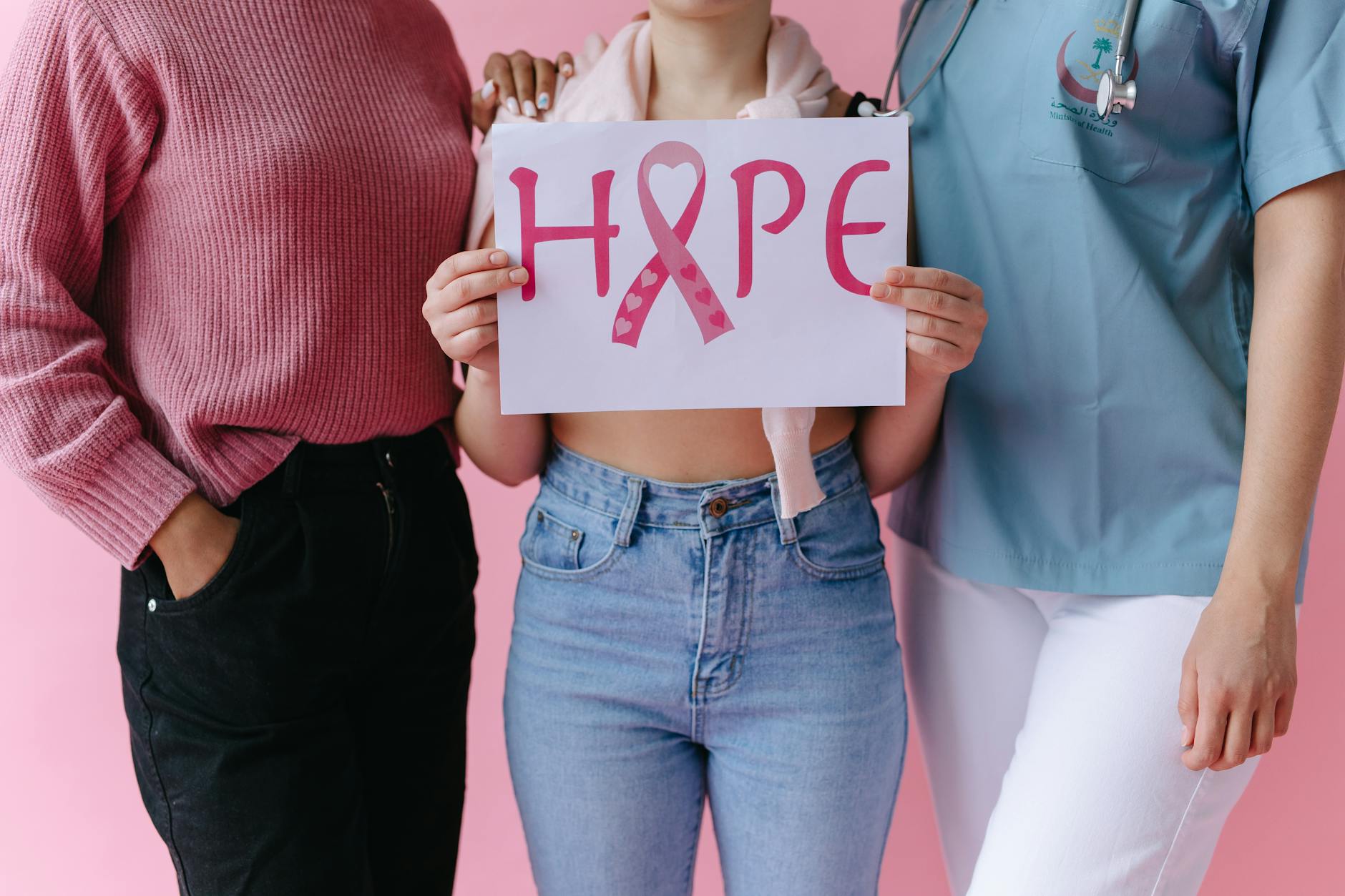 Three women holding a 'HOPE' sign with a pink ribbon for breast cancer awareness.