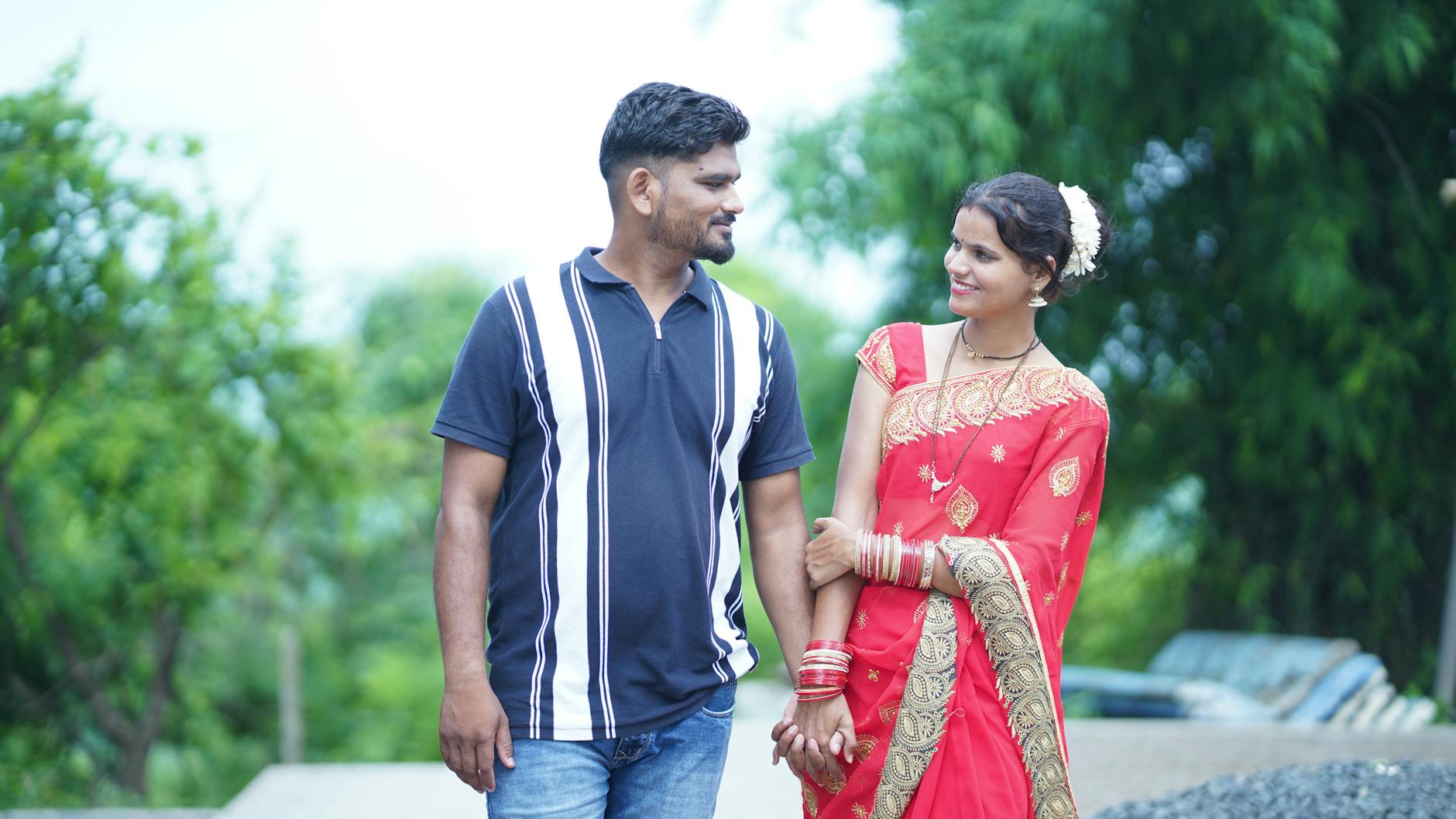 Smiling couple holding hands outdoors, showcasing love and togetherness in traditional clothing.