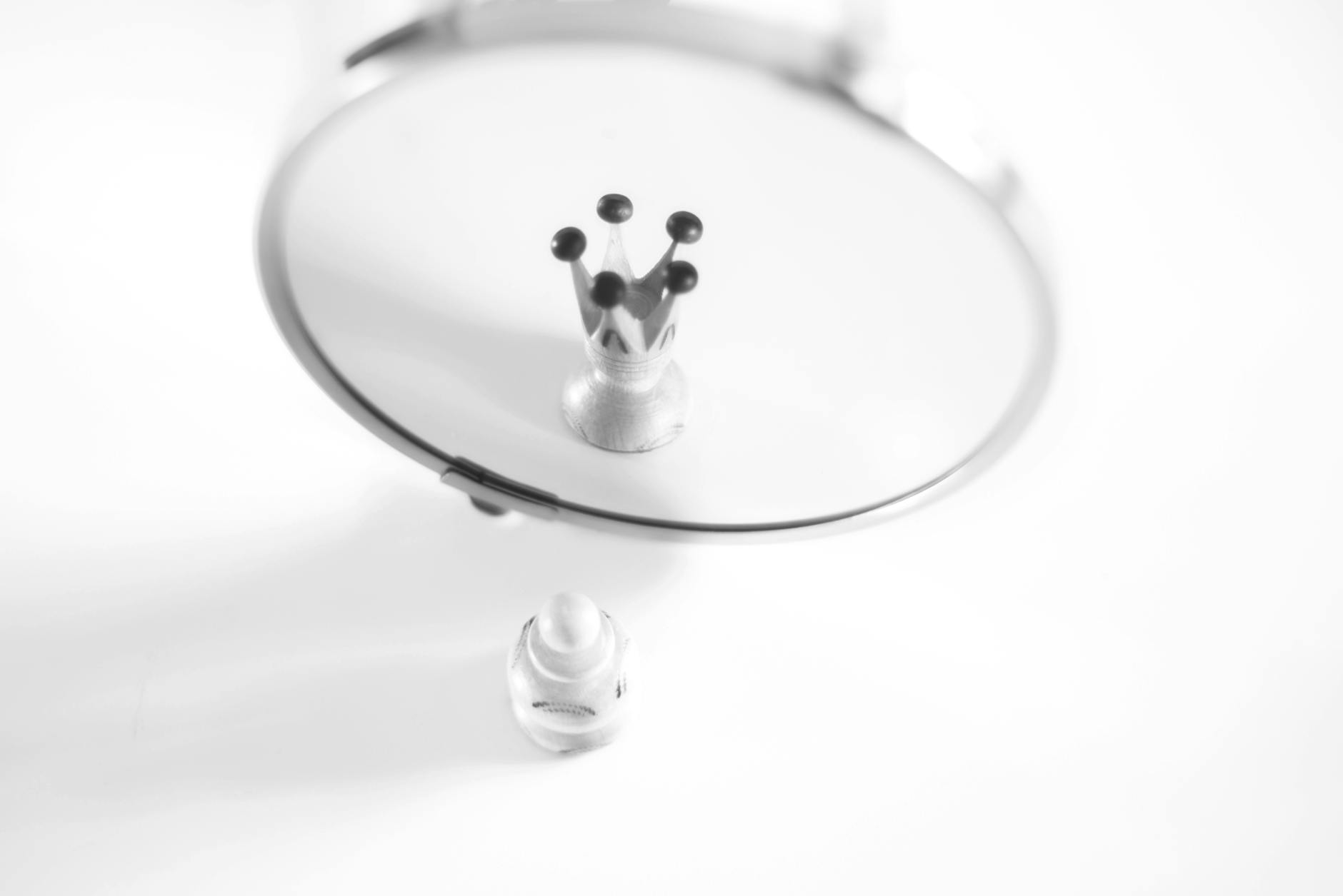 A creative black and white image showing a pawn's reflection as a crown, symbolizing self-perception.
