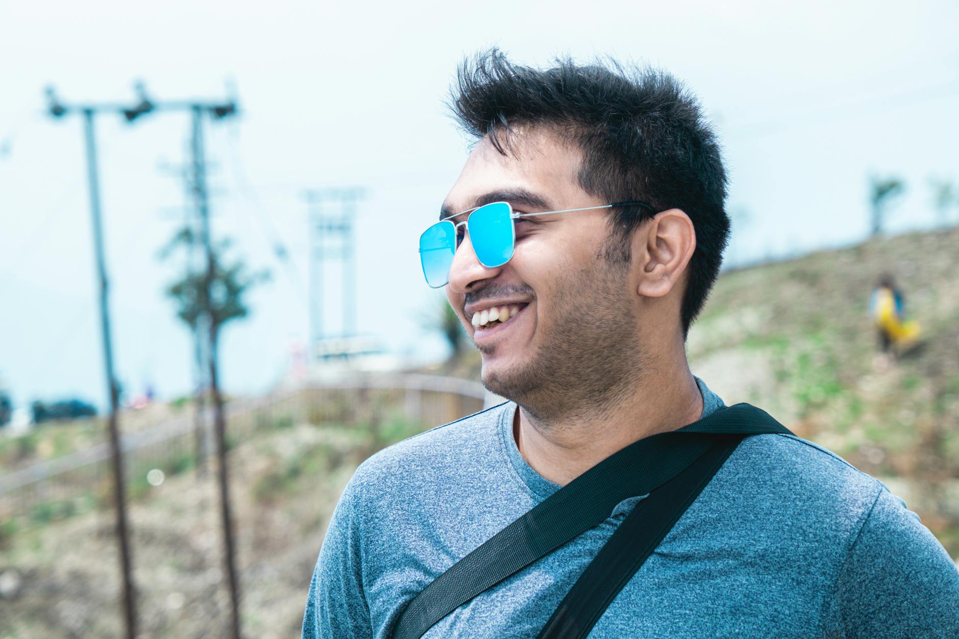 Smiling young man with sunglasses enjoying a sunny day outdoors. Casual fashion and cheerful mood.