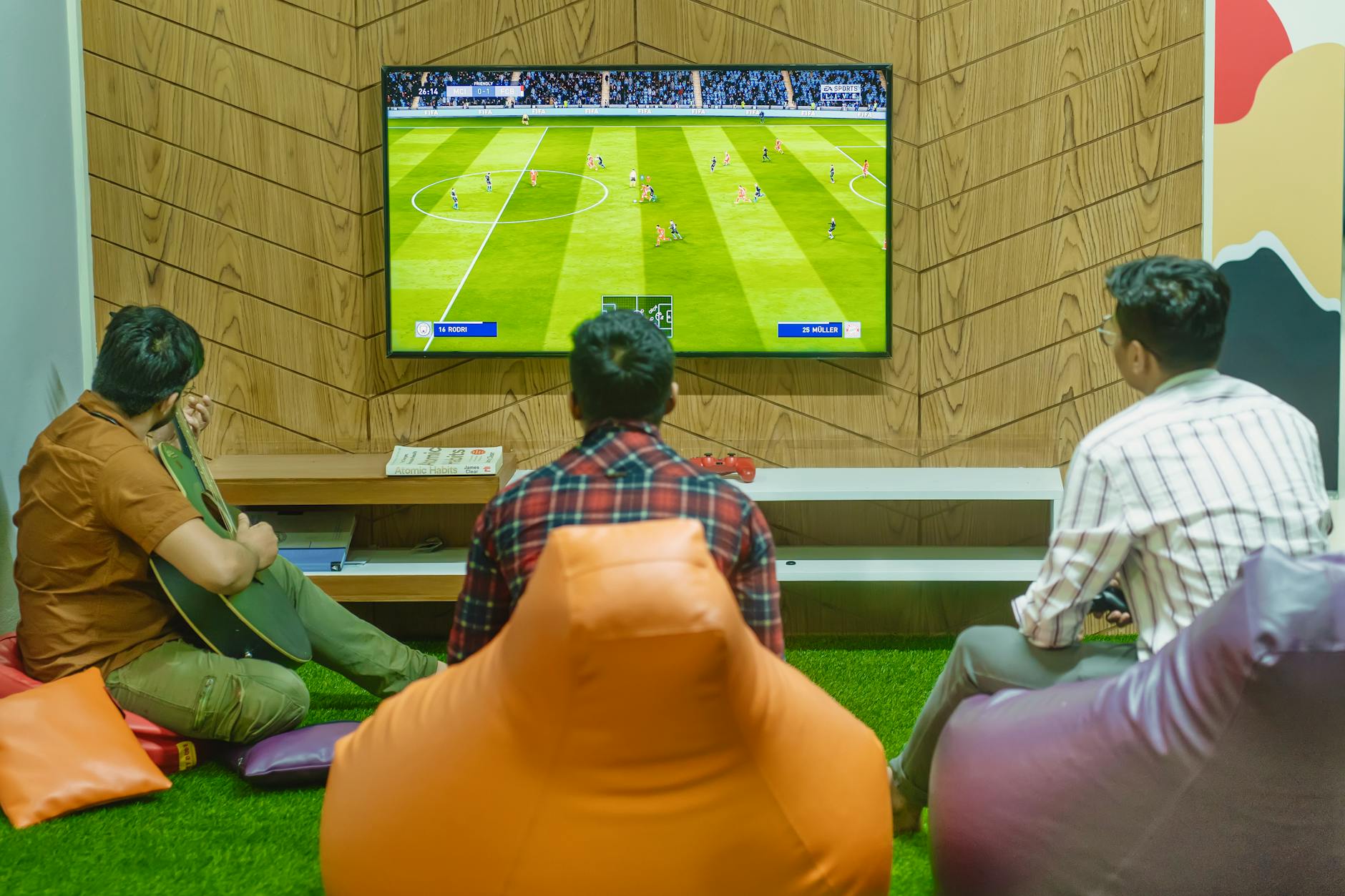 Three friends relaxing and playing a soccer video game indoors on a comfortable game night.